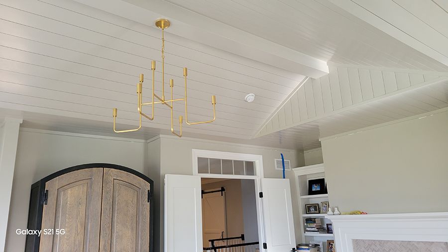Gold chandelier hangs from a white paneled ceiling with a light gray wall and a wooden cabinet.