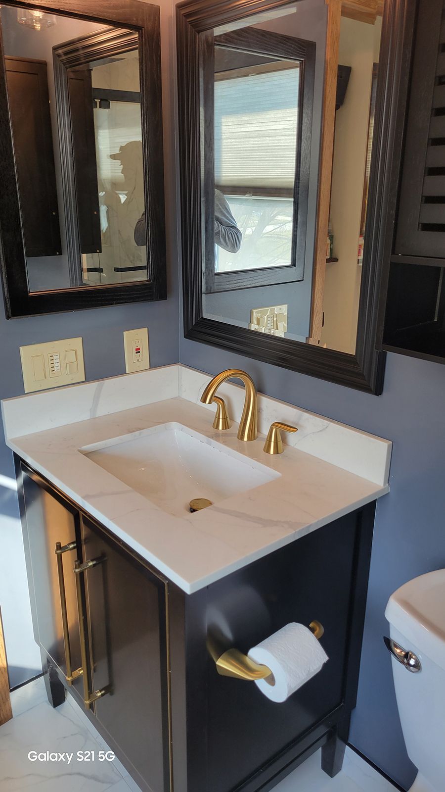 Bathroom with black vanity, white countertop and sink, gold fixtures, and two mirrors.