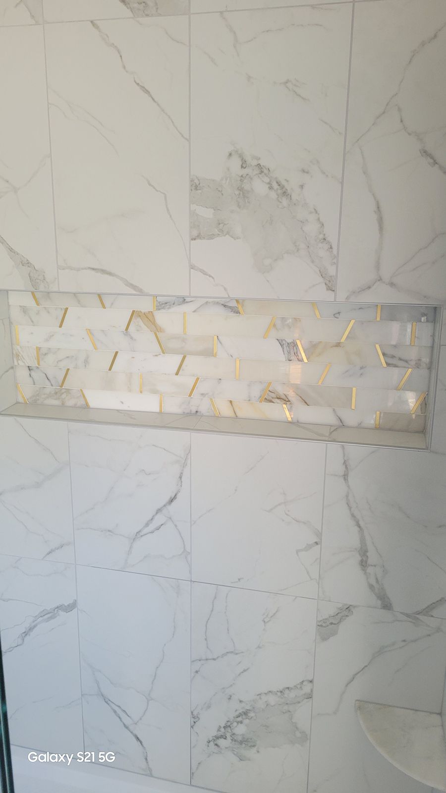 White marble tiled shower with recessed shelf of mixed beige tiles.
