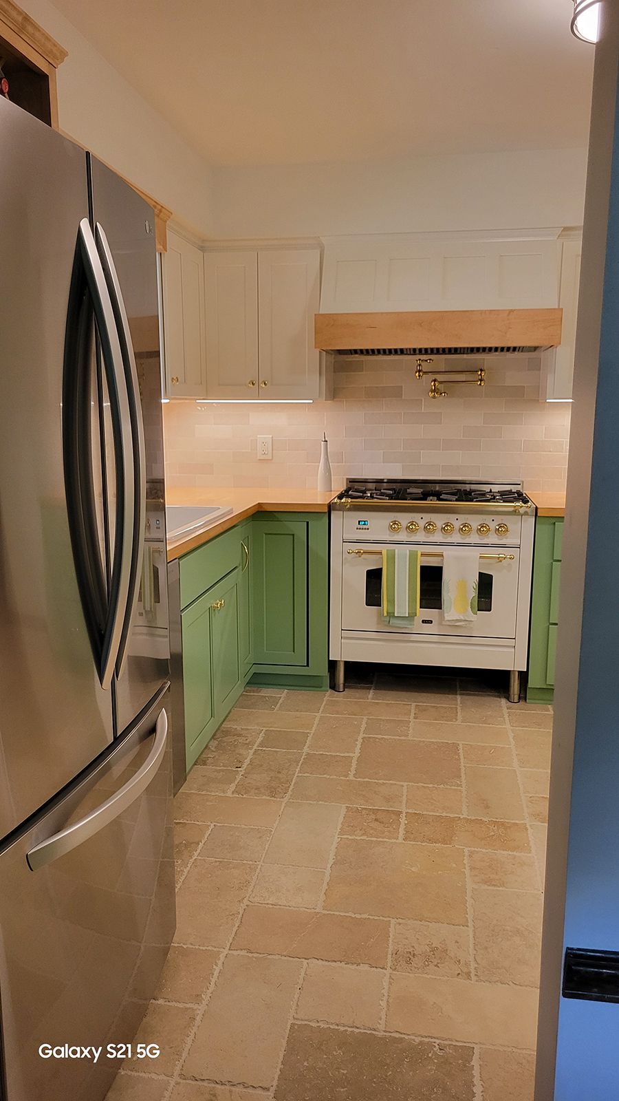 A kitchen with sage green and cream cabinets, a stainless steel refrigerator, and a vintage-style stove.
