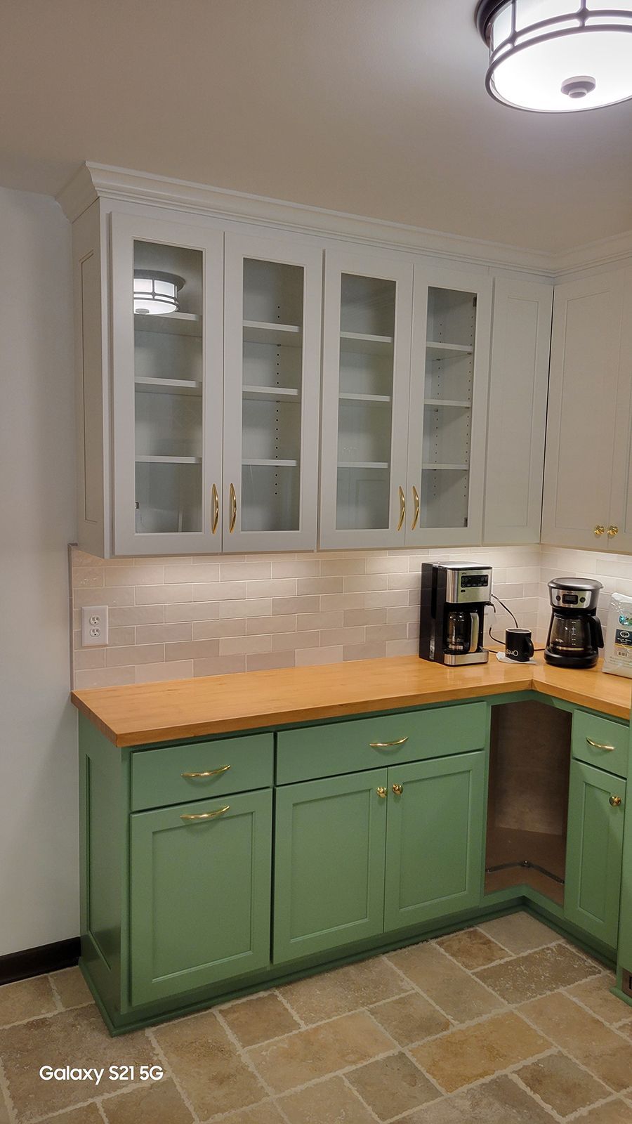 Green and white kitchen cabinets with glass-fronted upper cabinets, wood countertops, and tiled backsplash.