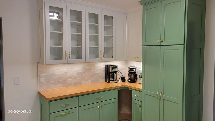 Green and white kitchen cabinets with wooden countertops and two coffee makers.