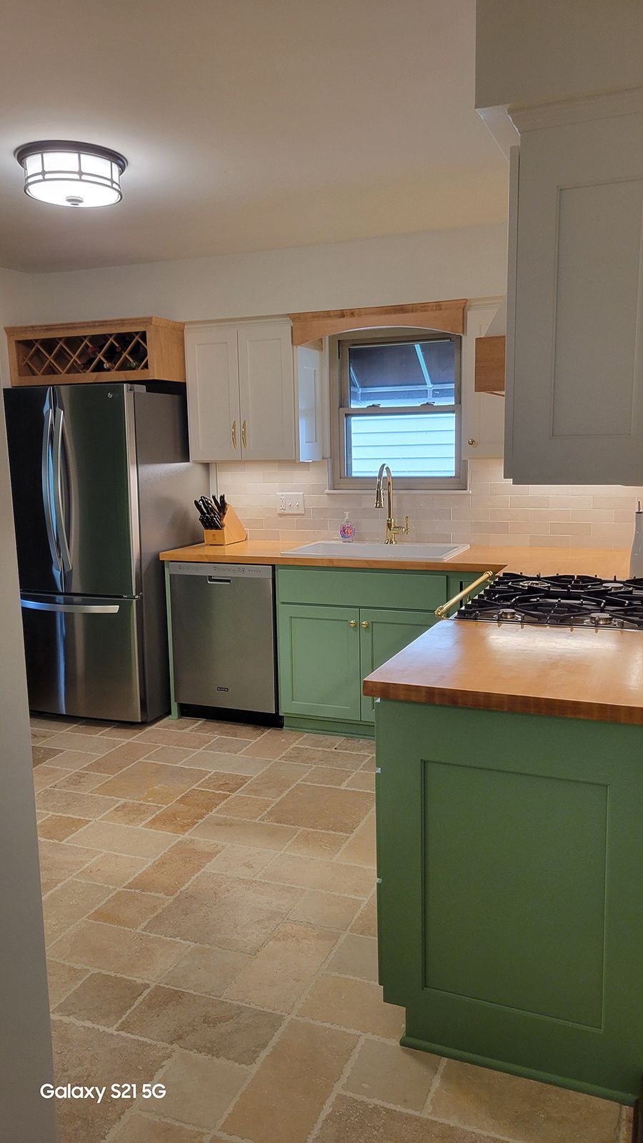 Kitchen with green and white cabinets, stainless steel appliances, and wood countertops.