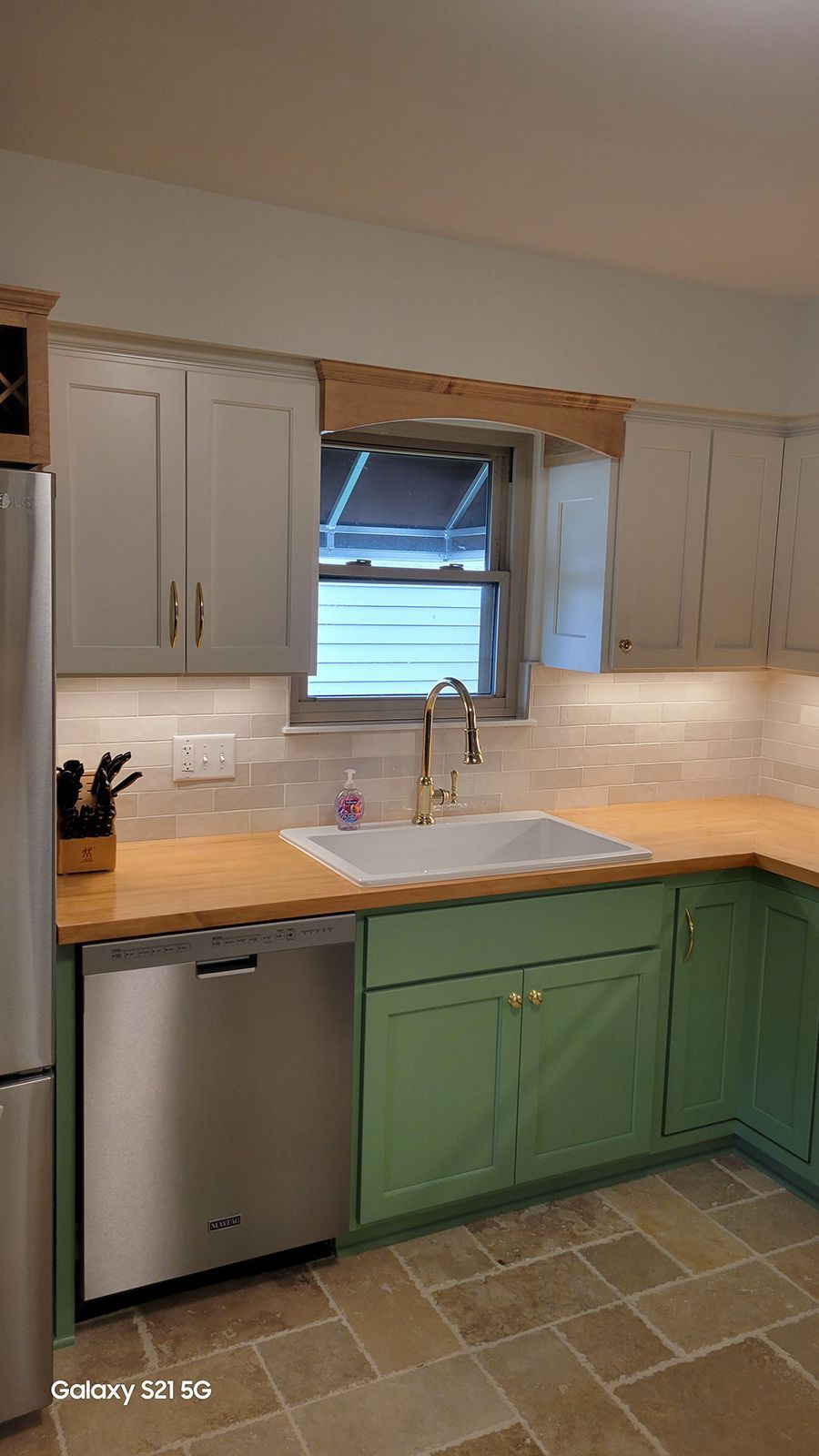 Kitchen with light gray and green cabinets, stainless steel appliances, wood countertop, and window.