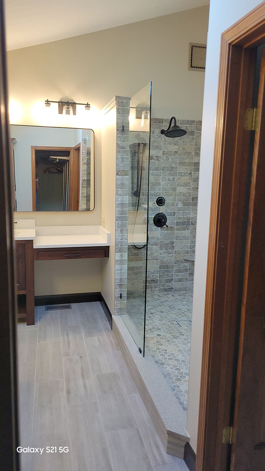Bathroom with a walk-in shower. Gray tile shower wall. Glass shower door. Wooden vanity.