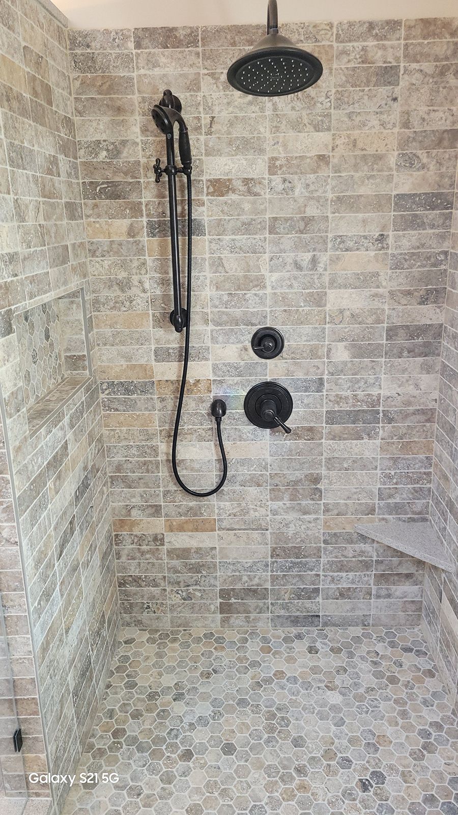 Shower with gray stone tile, black fixtures, and built-in bench.