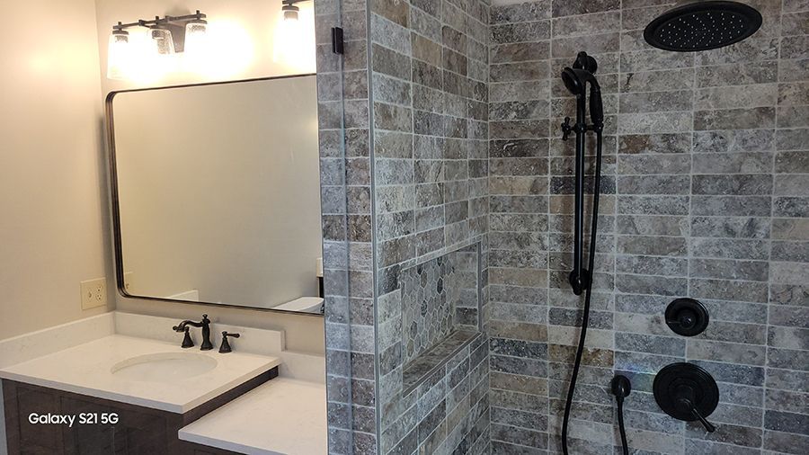 Bathroom with gray tile shower, black fixtures, white countertop, and mirror.