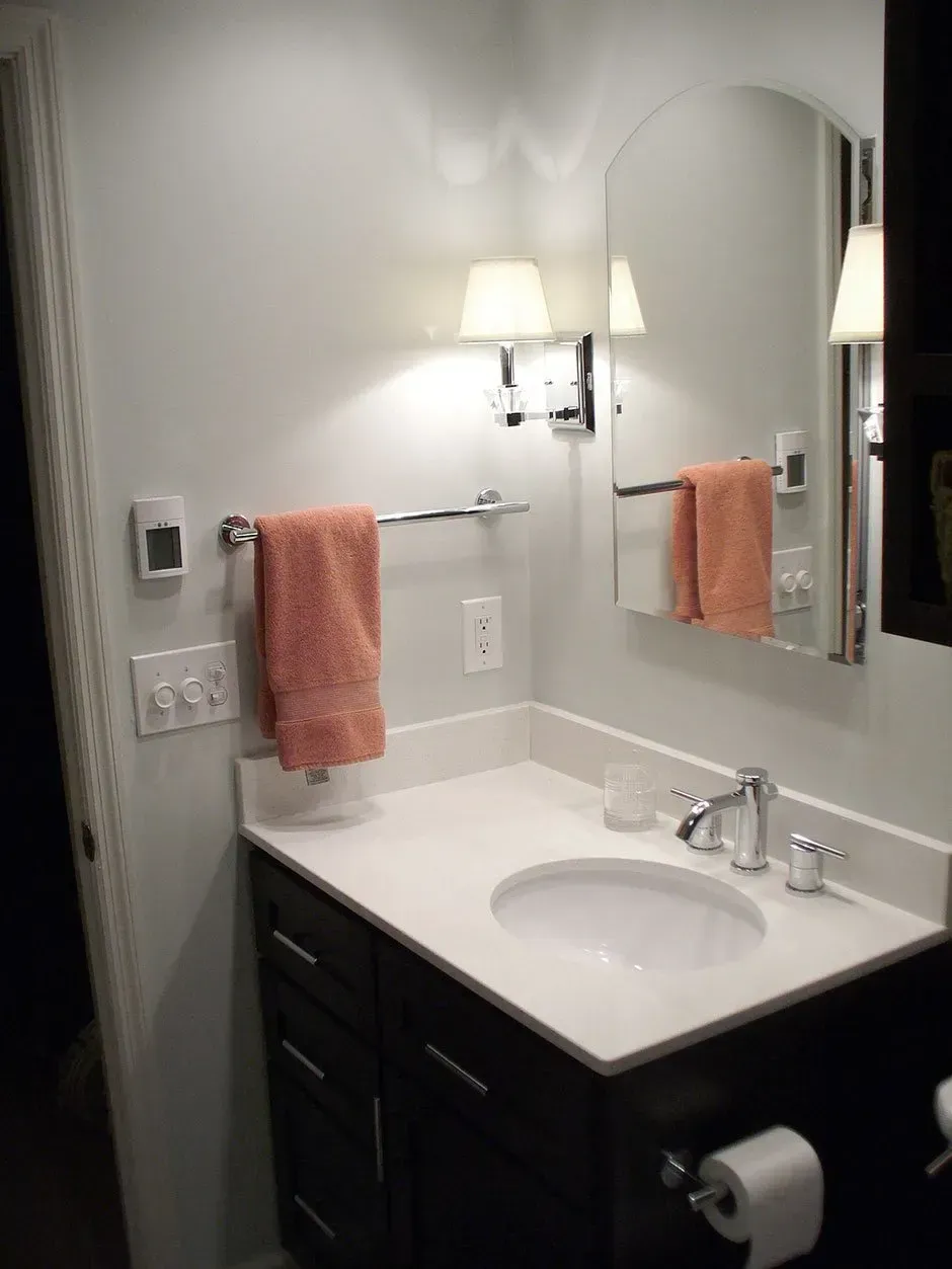 Bathroom with white countertop, dark cabinets, peach towels, and arched mirror.