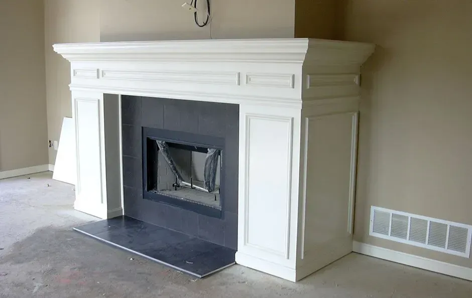 White fireplace mantel with dark tiled surround and hearth in an unfinished room.
