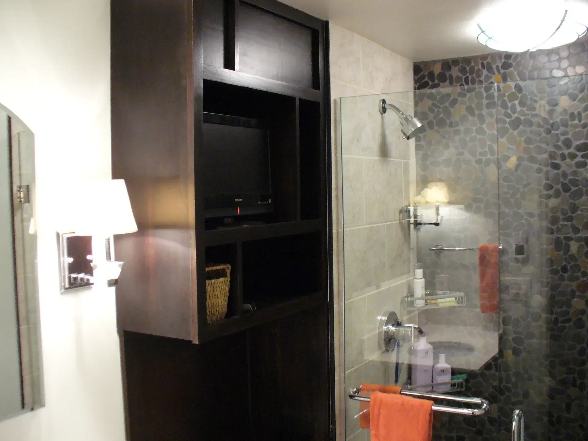 Bathroom with dark cabinetry, shower, and a TV.