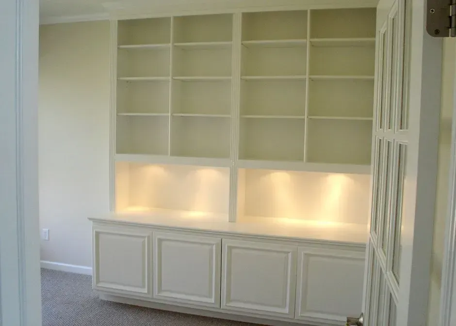 White built-in bookshelves with cabinet storage and recessed lighting in a room, viewed from a doorway.
