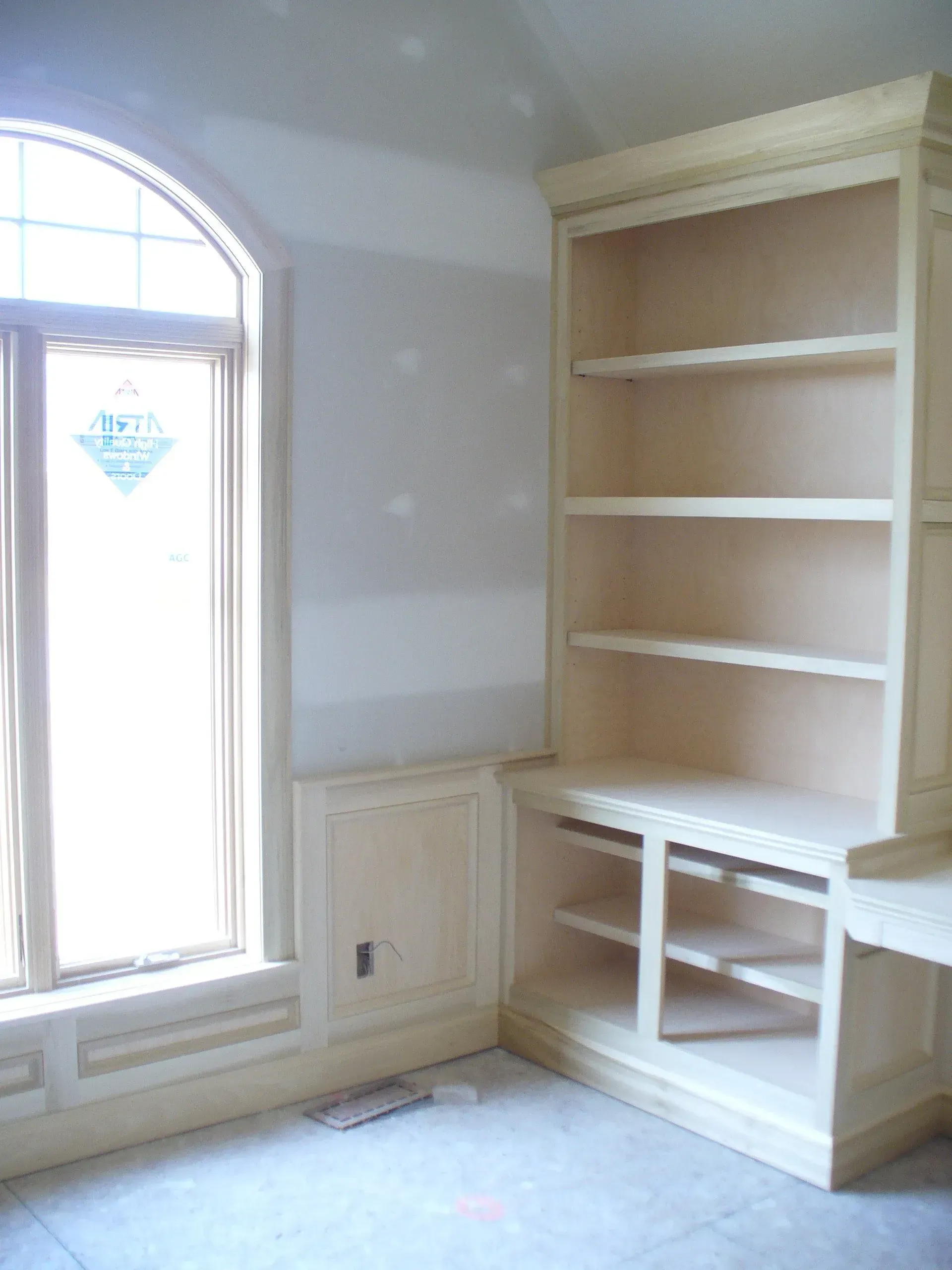 Built-in wooden bookcase and desk with an arched window on the left.