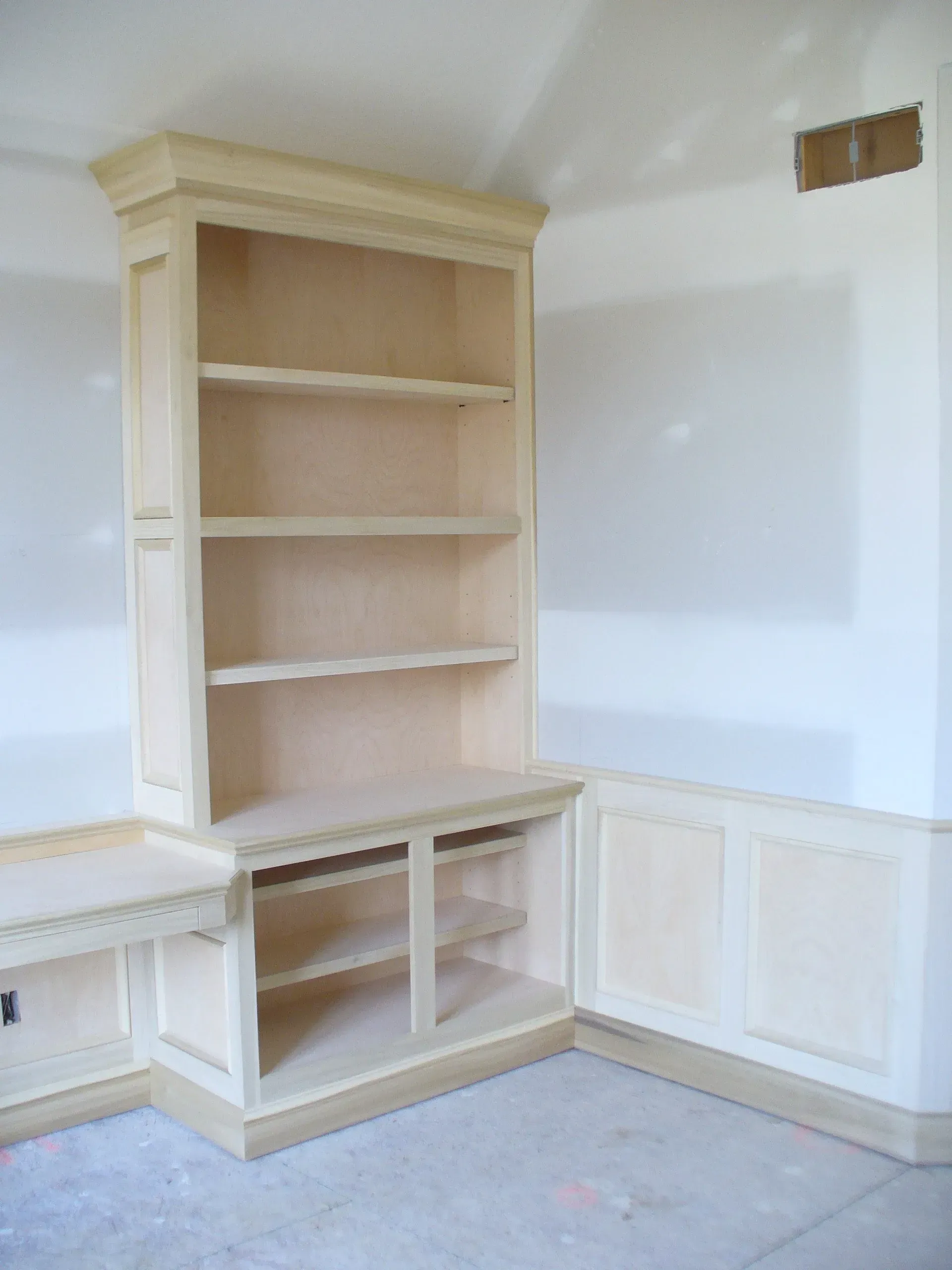 Built-in wooden bookcase with shelves, unfinished, installed in a corner, with a desk section.