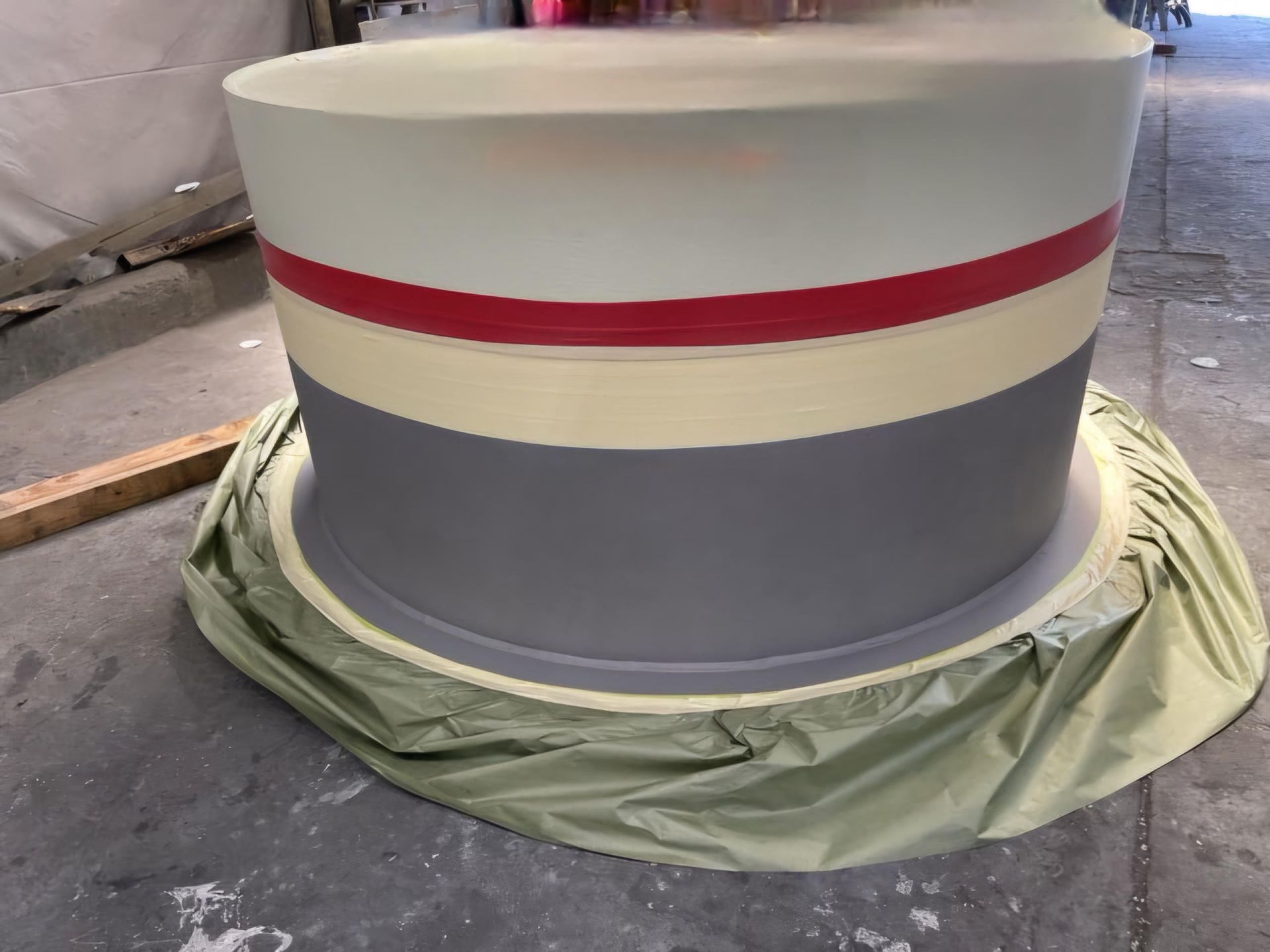 Large painted cylindrical tank with cream, red, and gray bands, sitting on a covered floor.