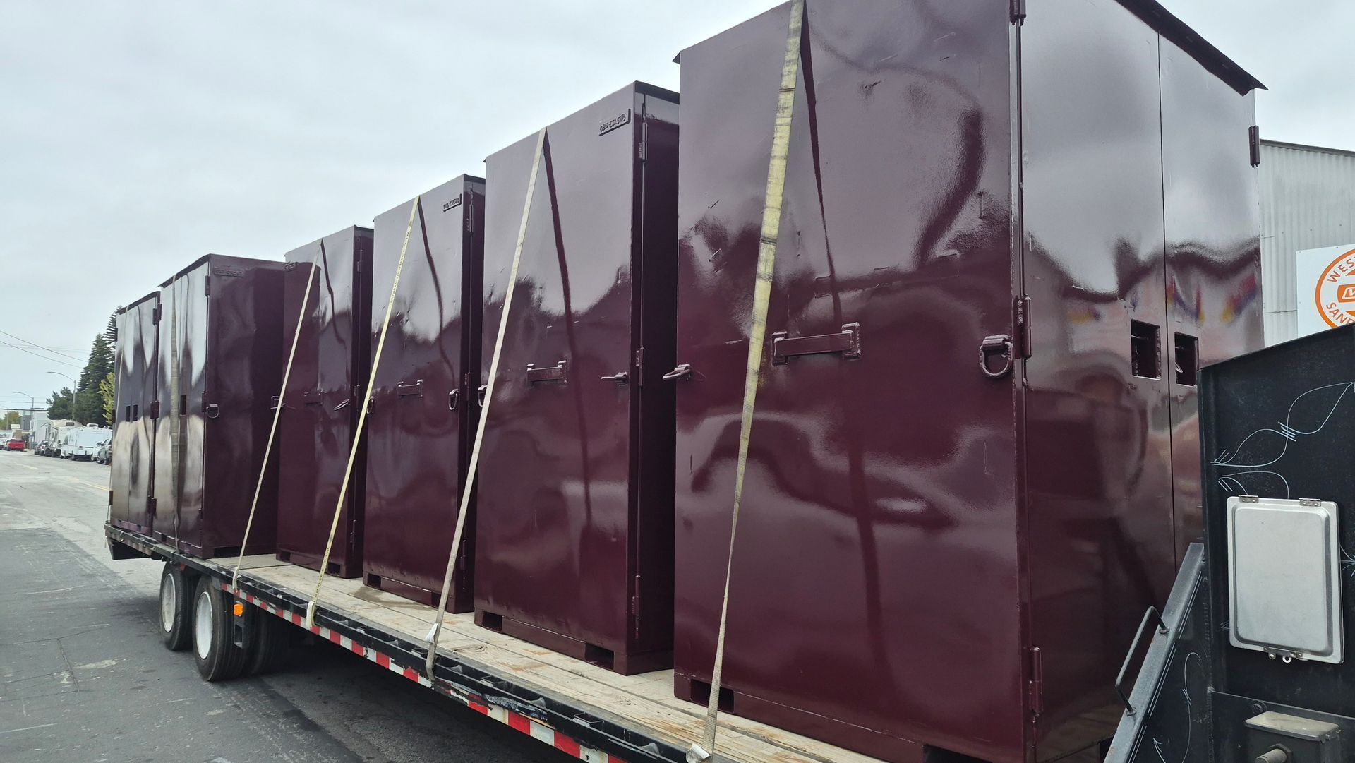Maroon modular buildings strapped on a flatbed trailer beside a roadside