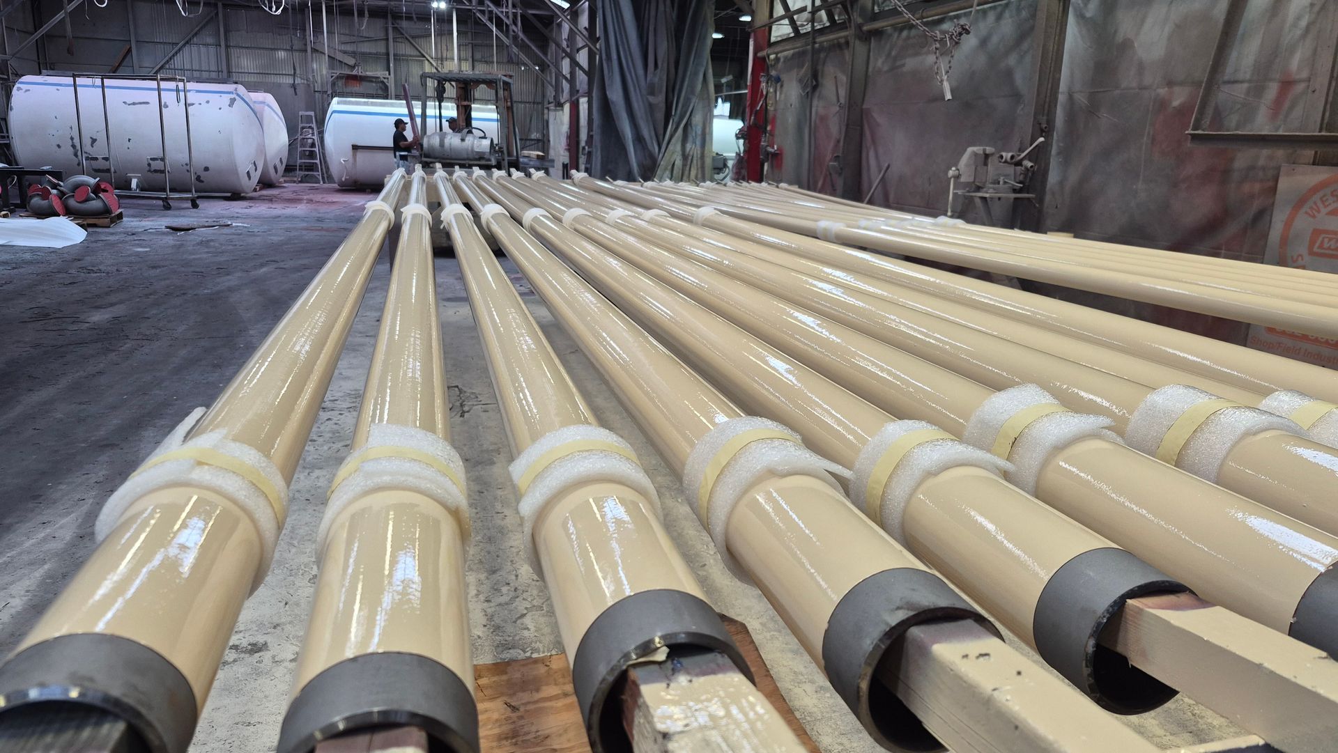Long tan industrial pipes laid in rows inside a factory or utility tunnel.