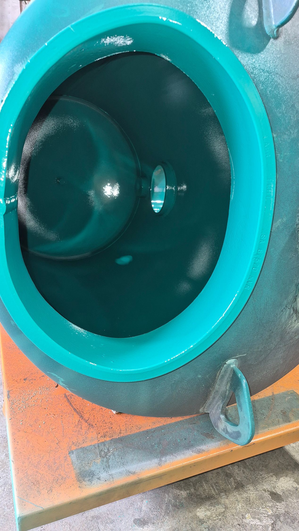Close-up of a teal industrial pipe opening with a dark interior and metal fittings beneath it