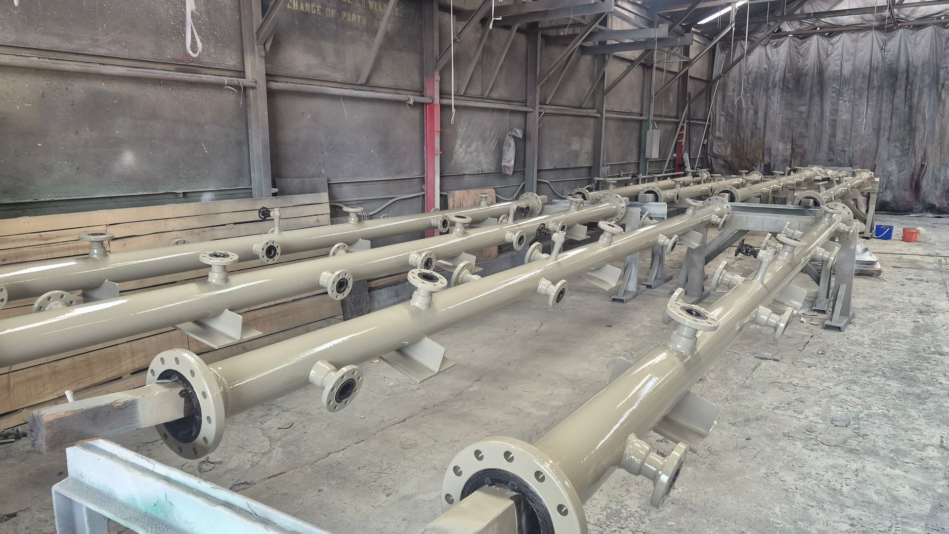 Rows of tan industrial pipes with flanges stored in a warehouse or workshop.