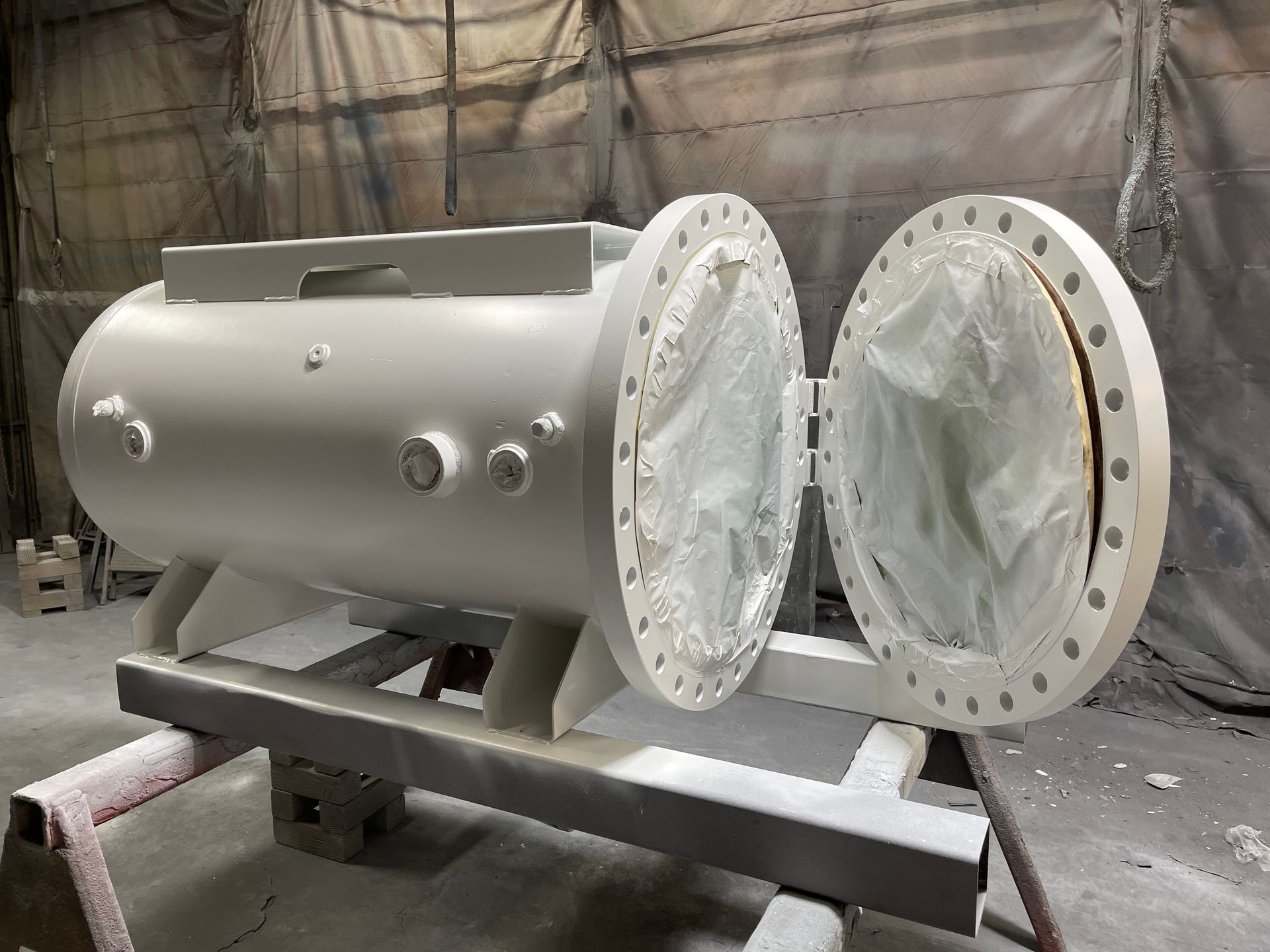 Large gray industrial pressure vessel with open flanged ends on a metal stand in a workshop.