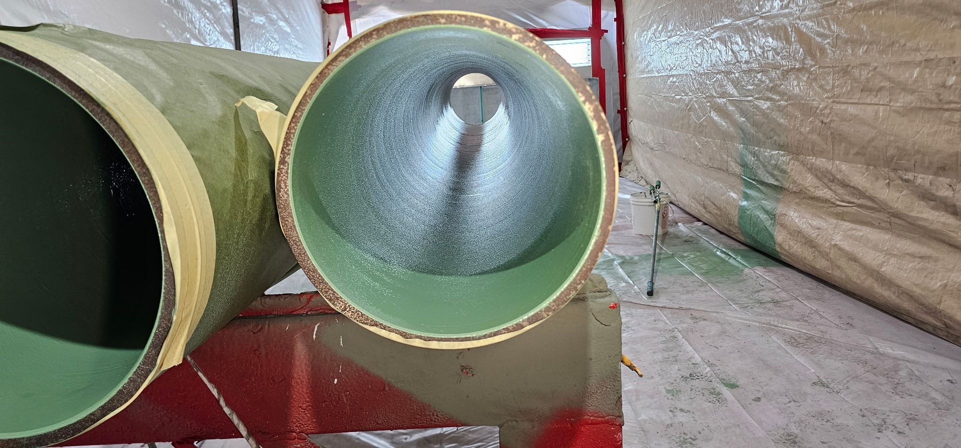 Two large green metal ducts, one with a conical insert, resting on a red floor indoors.