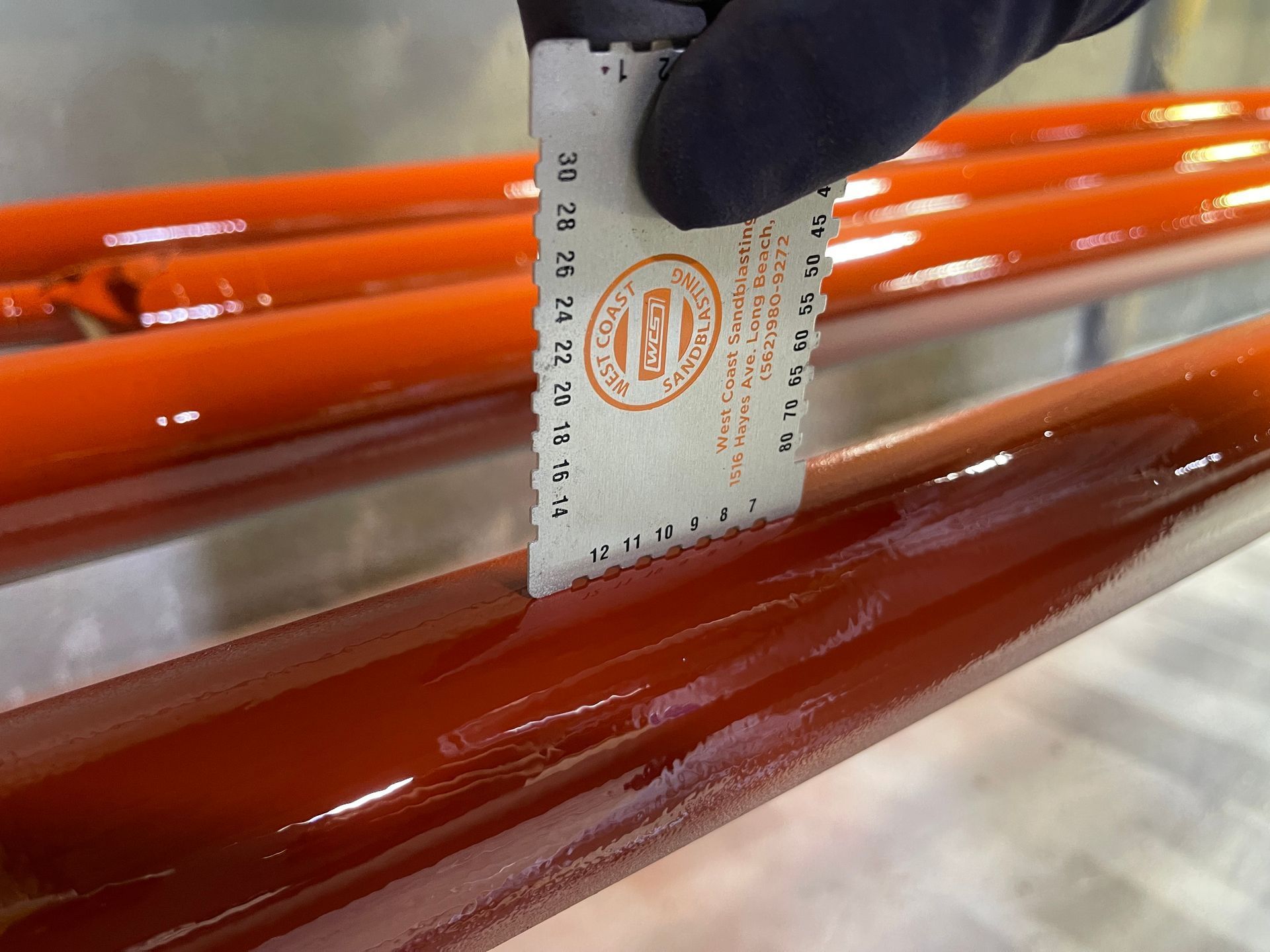 Gloved hand using a ruler to measure the width of glossy orange tubes and a brown tube