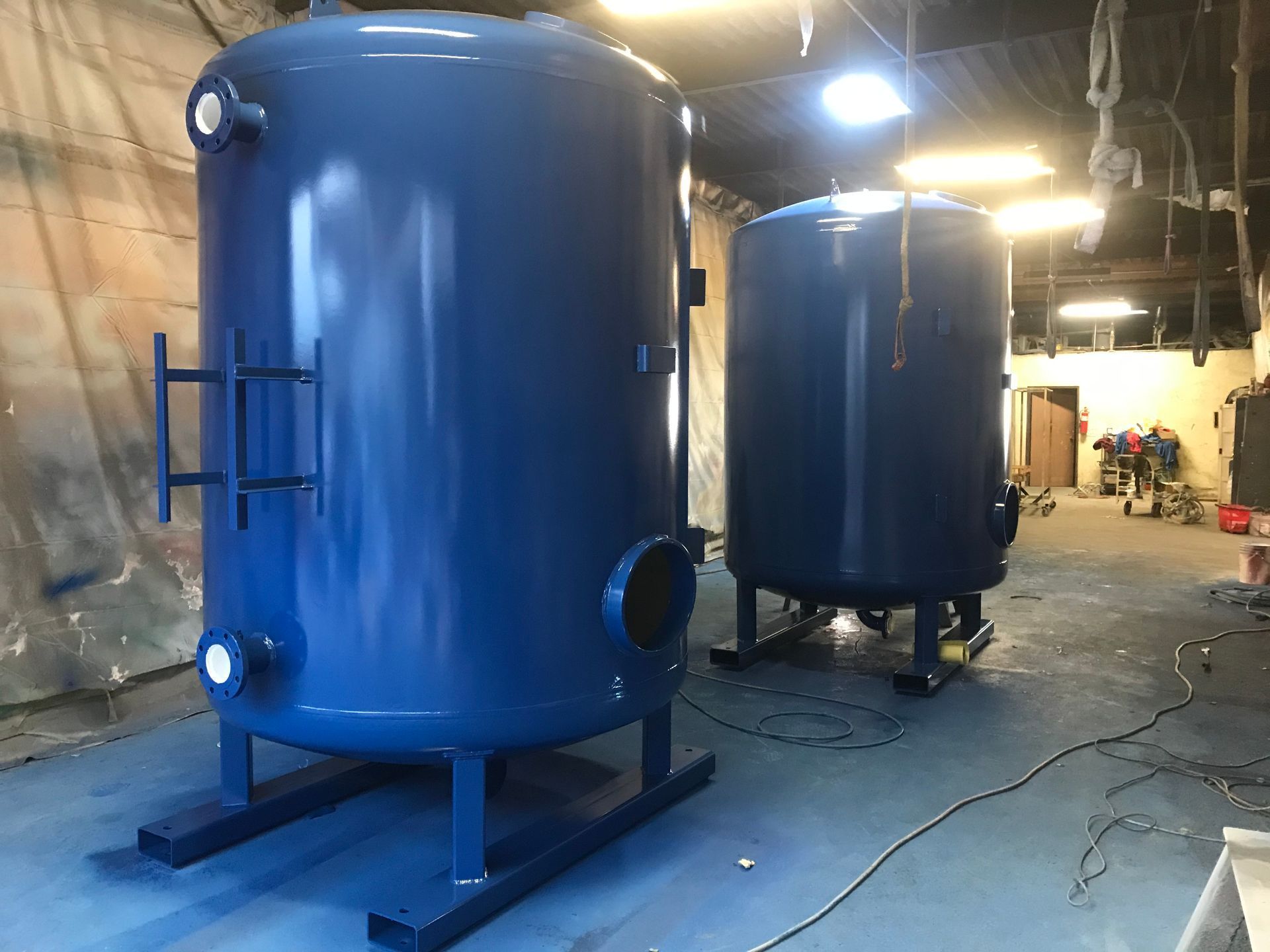 Blue industrial tanks in a workshop, one large tank in the foreground and another behind it.