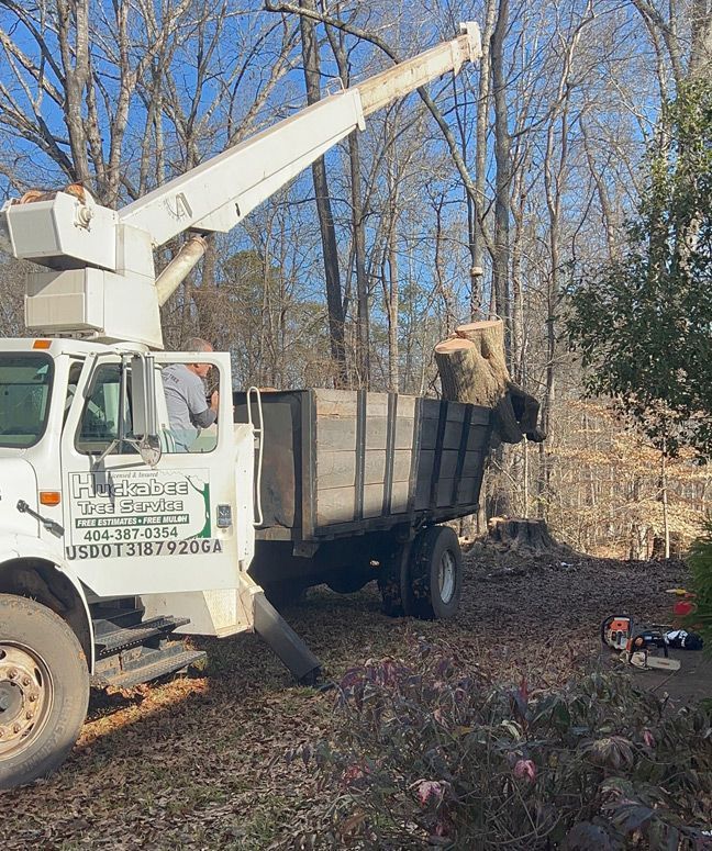 A white truck with a crane on top of it is parked in the woods.