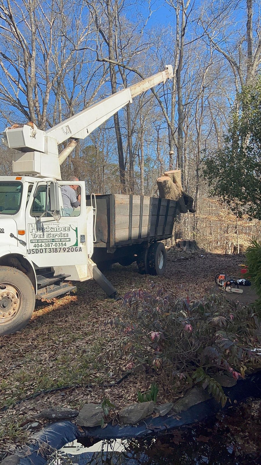 A white truck with a crane on top of it is parked in the woods.
