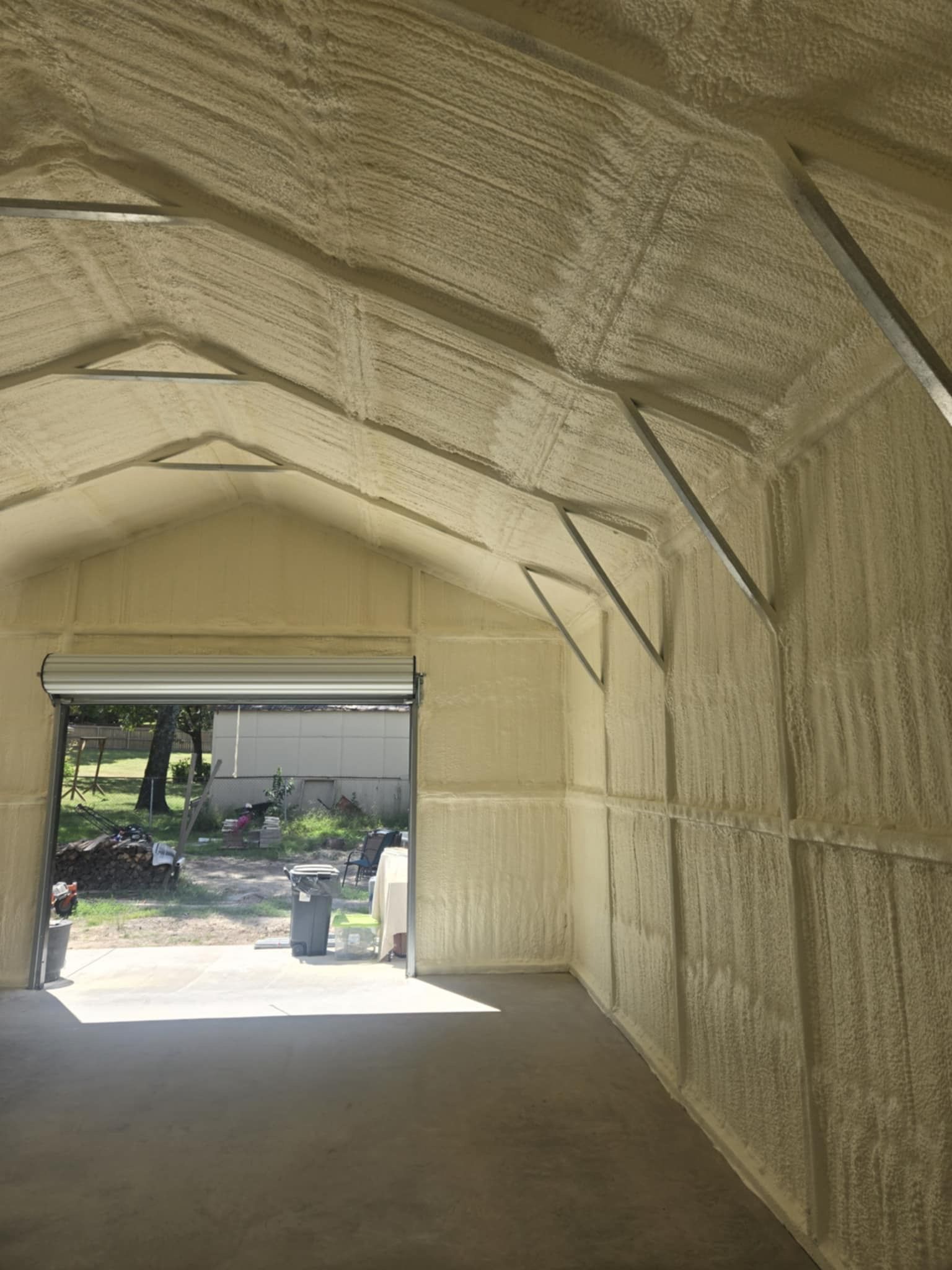 Interior view of a building with spray foam insulation on walls and ceiling, garage door open to exterior.