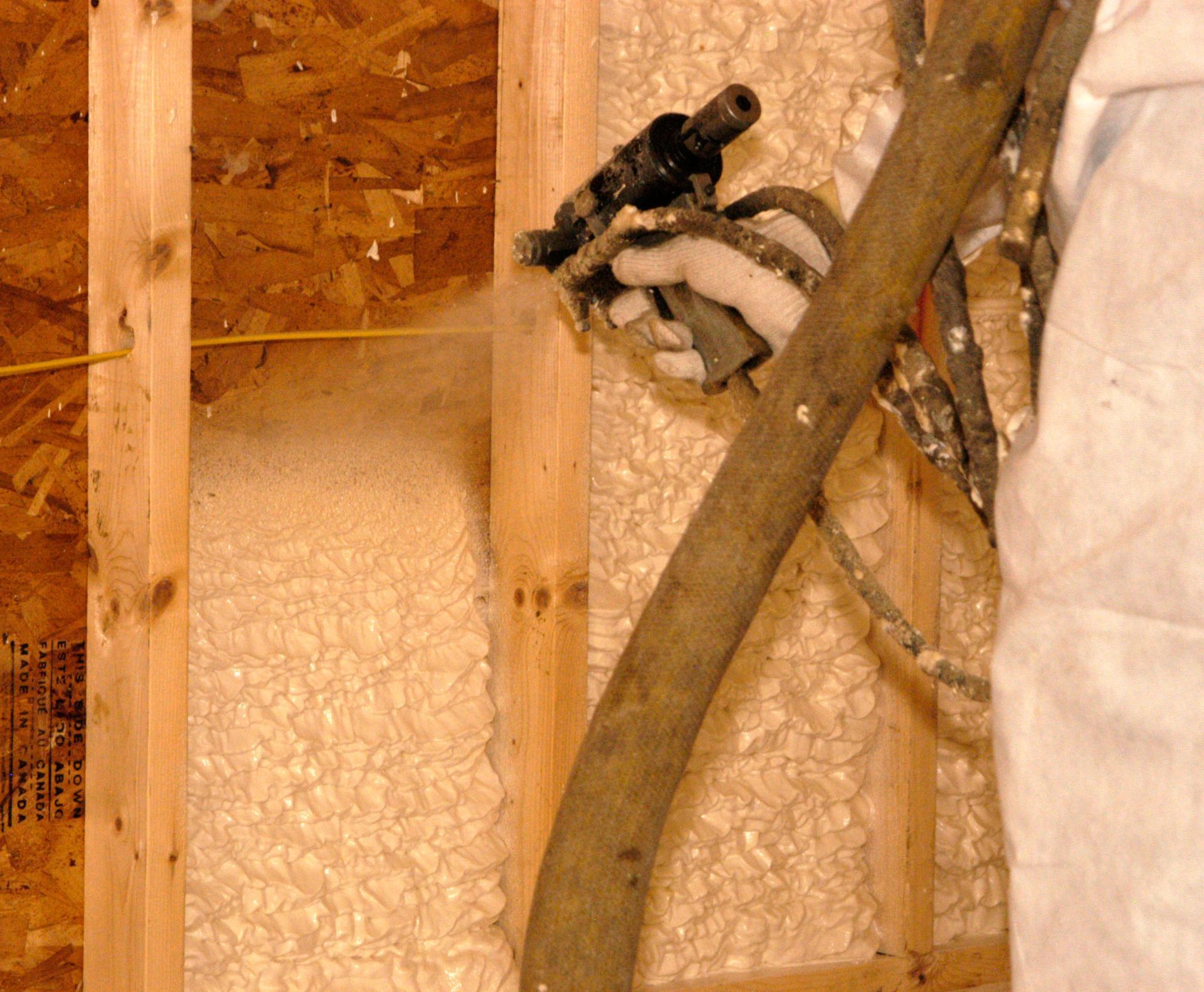 Spraying foam insulation into a wooden wall frame. A worker holds the sprayer.