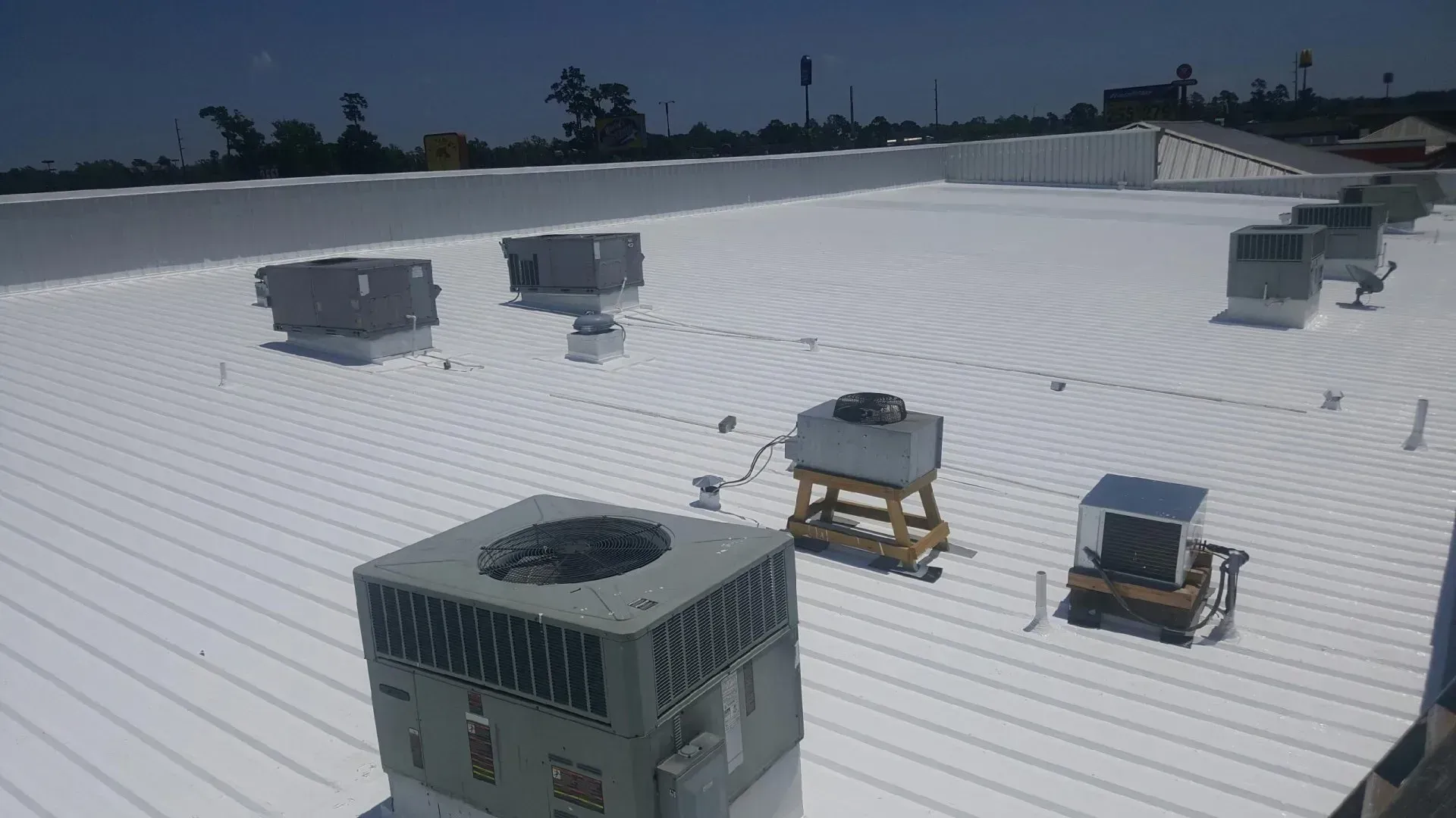 White commercial roof with HVAC units under a clear sky.