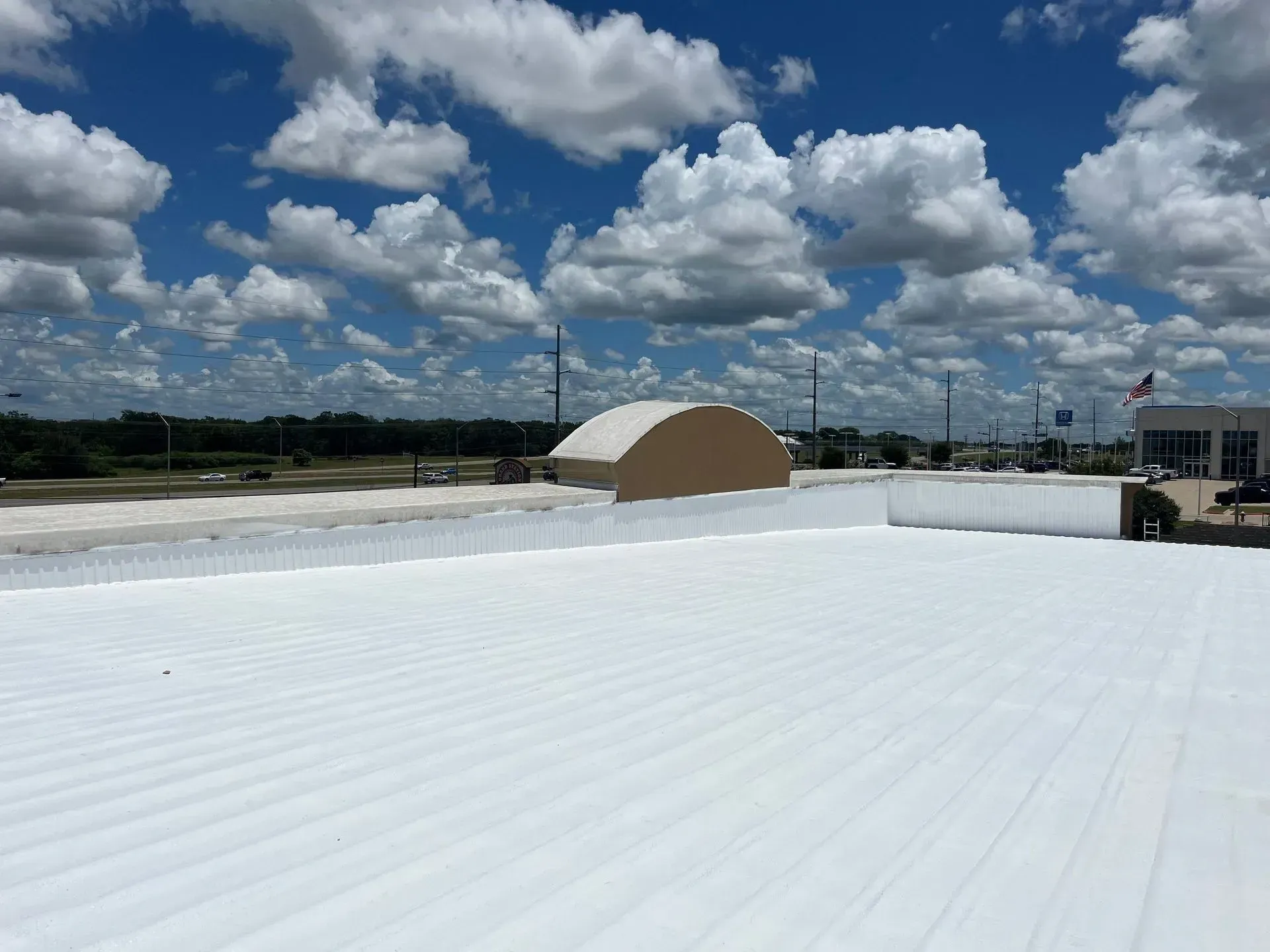 White roof with ribbed texture, blue sky with puffy white clouds.