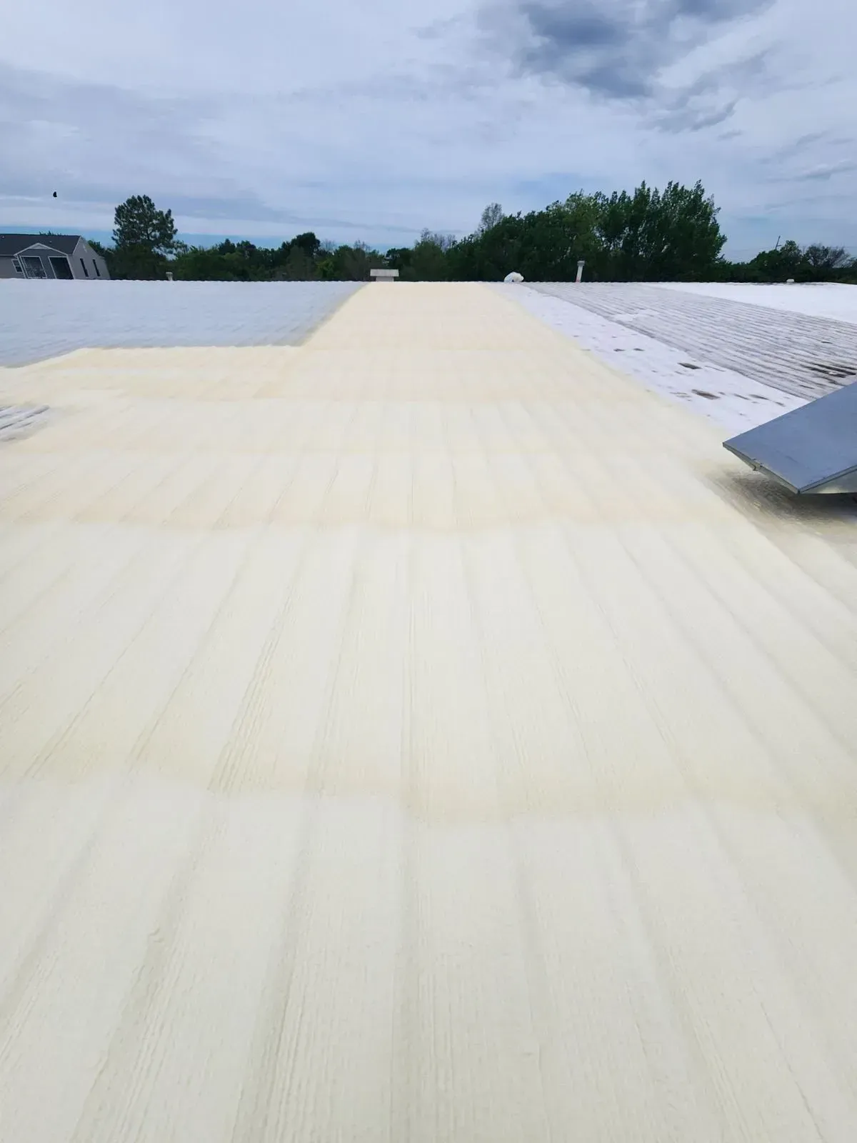 Flat roof with beige material being installed, cloudy sky overhead.