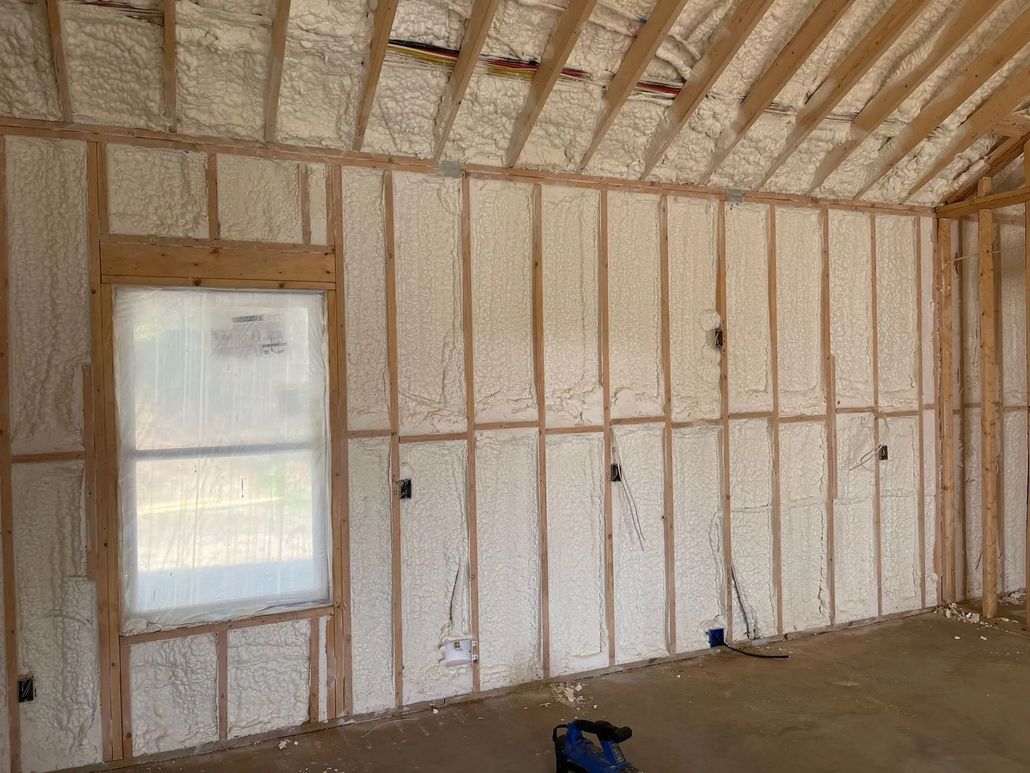 An interior view of a room under construction with spray foam insulation between wall studs and ceiling rafters.