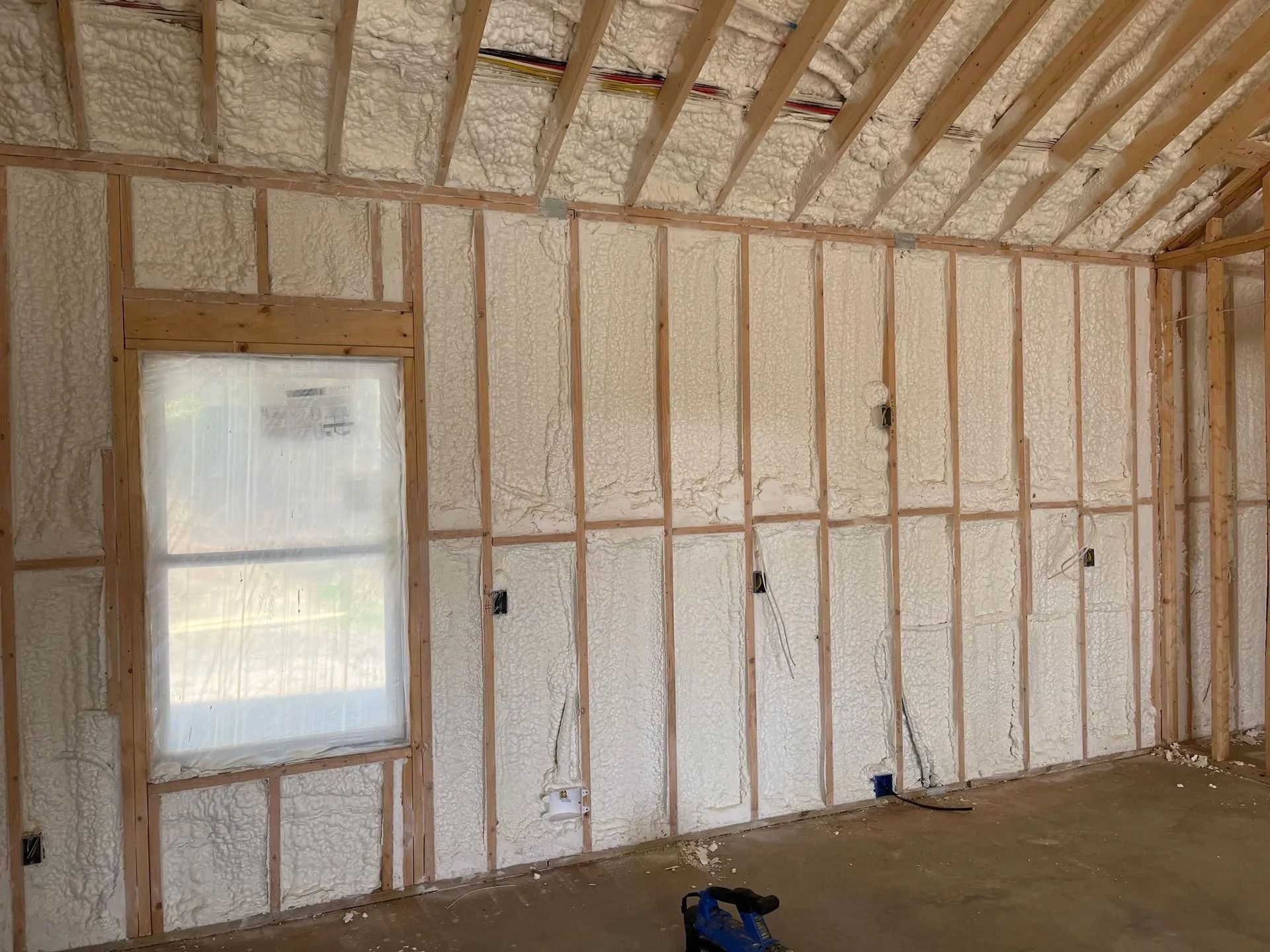 An interior view of a room under construction with spray foam insulation between wall studs and ceiling rafters.