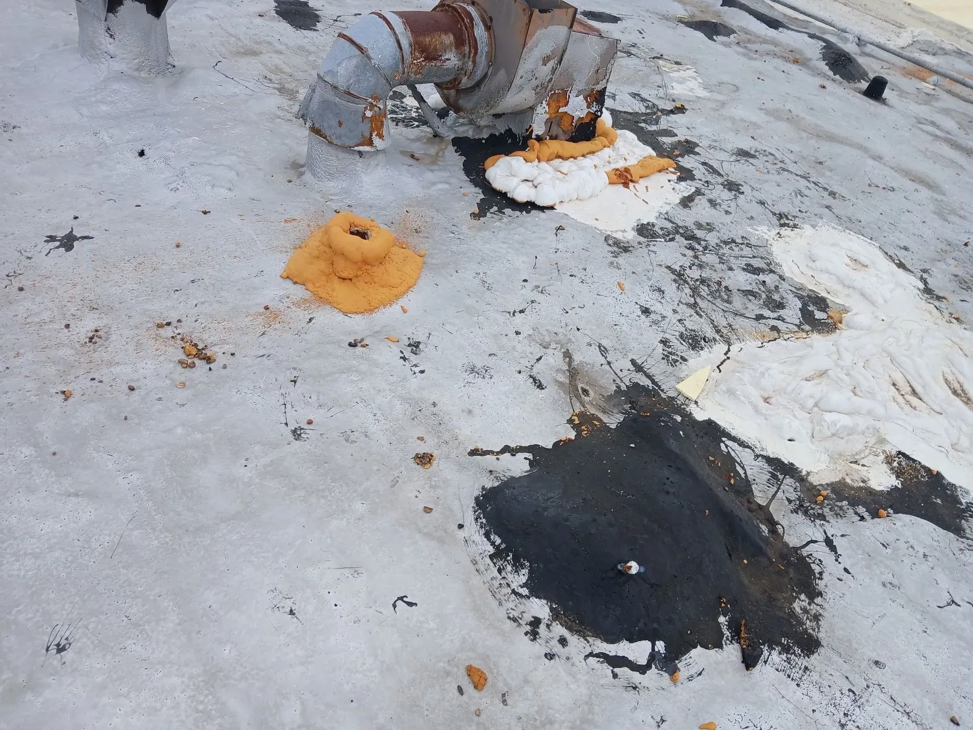 A weathered rooftop with pipe fittings and patches of repair sealant in various colors.