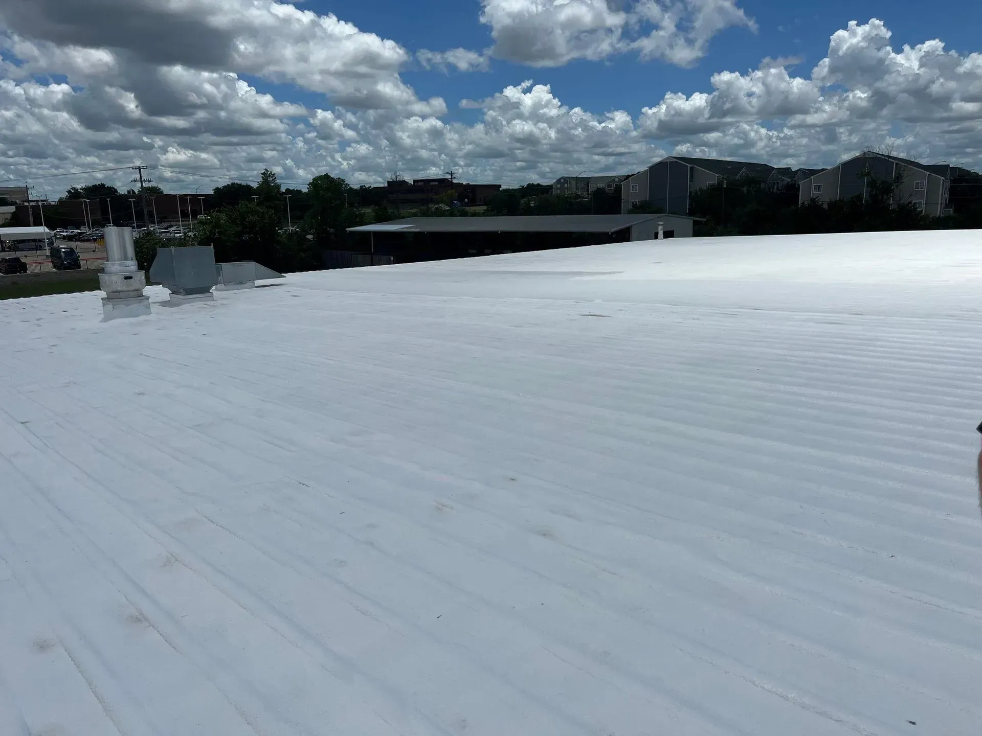 White metal roof with vents, cityscape in background, cloudy blue sky.