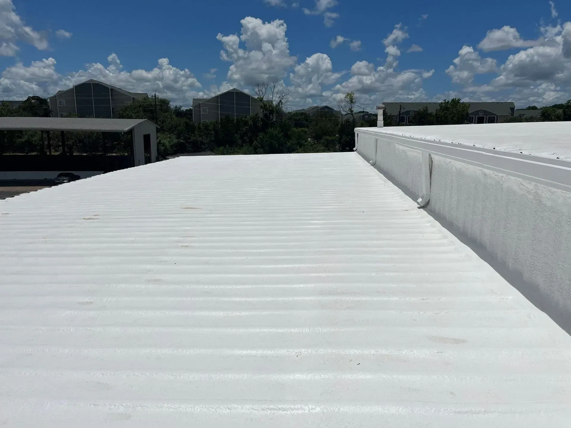 White coated corrugated metal roof with white trim, blue sky, and surrounding buildings.