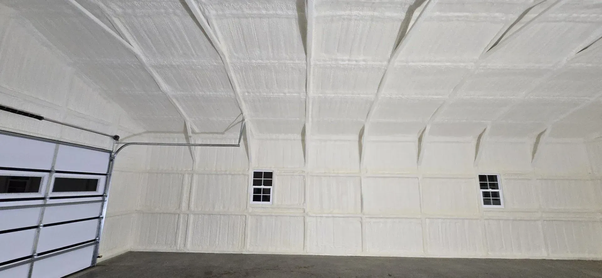 Interior view of a white insulated building with a garage door and two small windows.