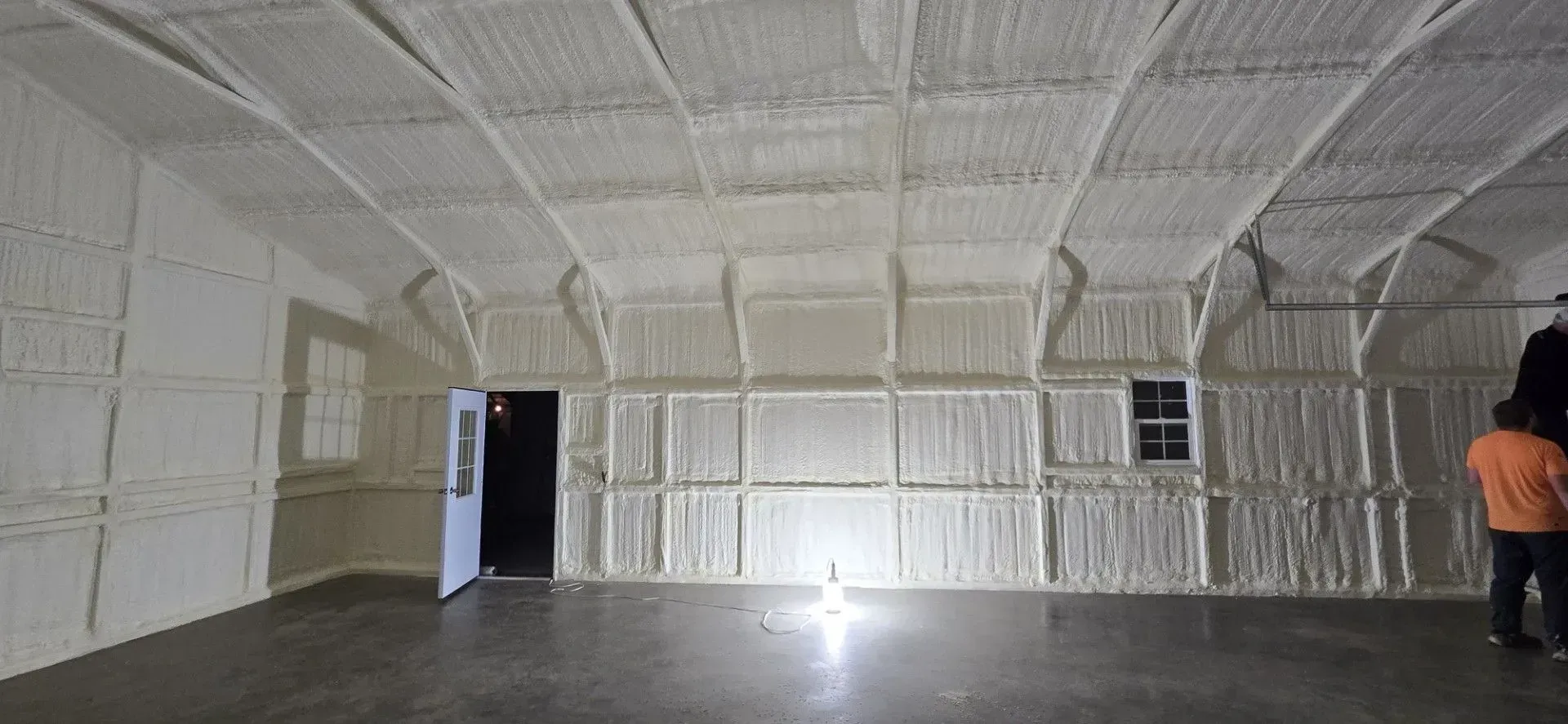 Interior view of a building with spray foam insulation on the walls and ceiling. A person stands near a door.