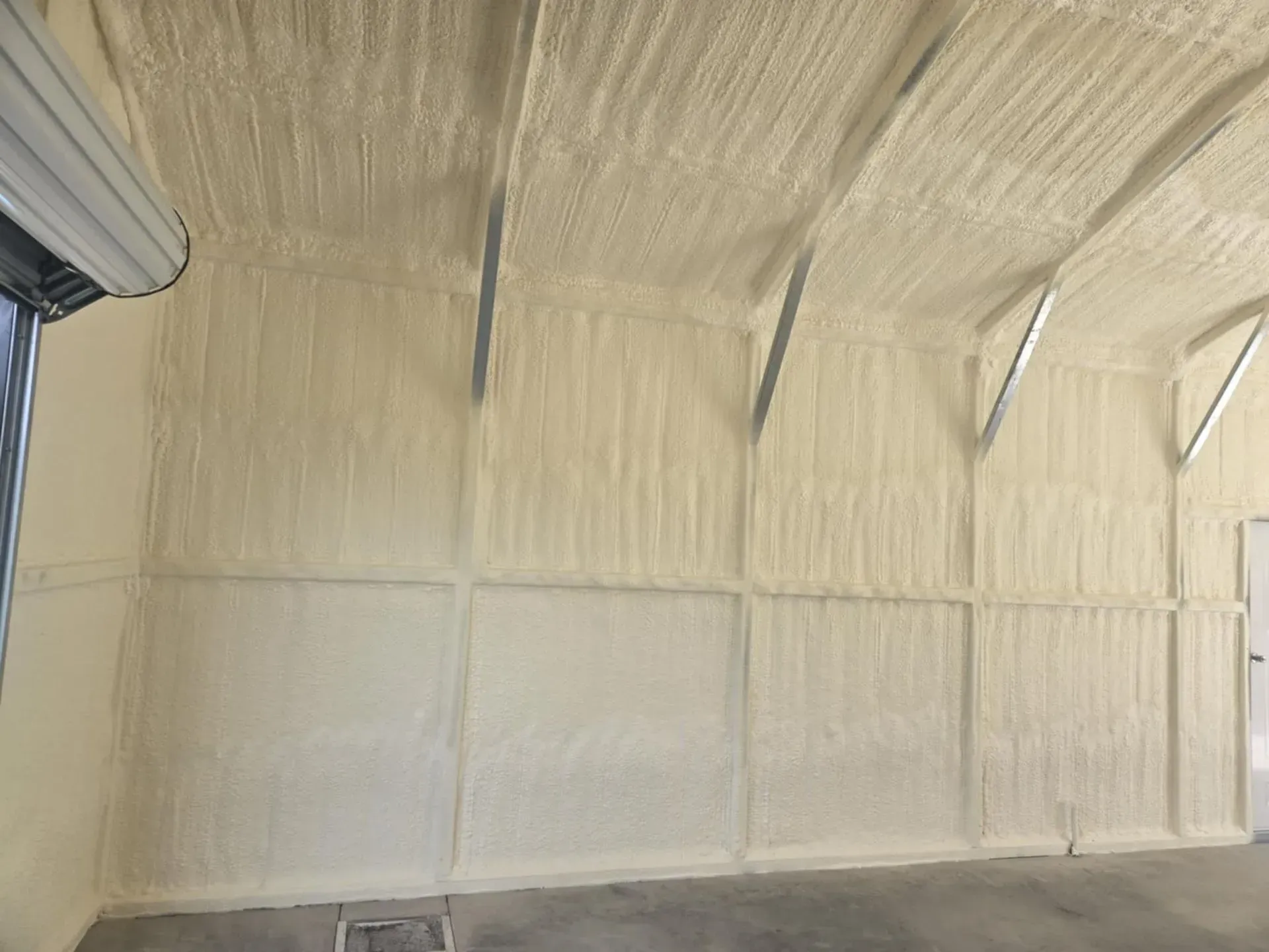 Interior of a building with spray foam insulation on the walls and ceiling, a metal door is partially visible on the left.