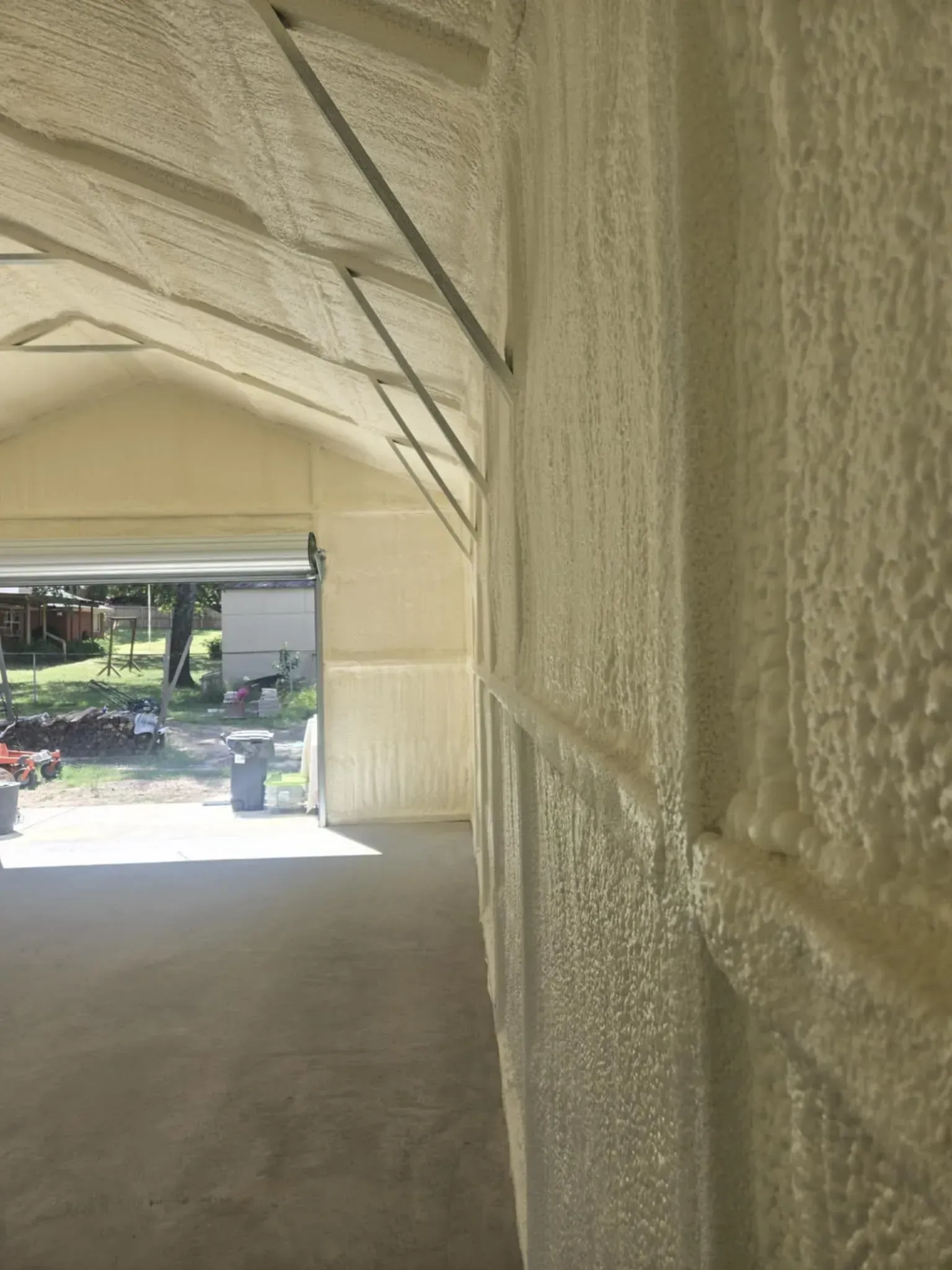 Garage interior with spray foam insulation, concrete floor, and open garage door.