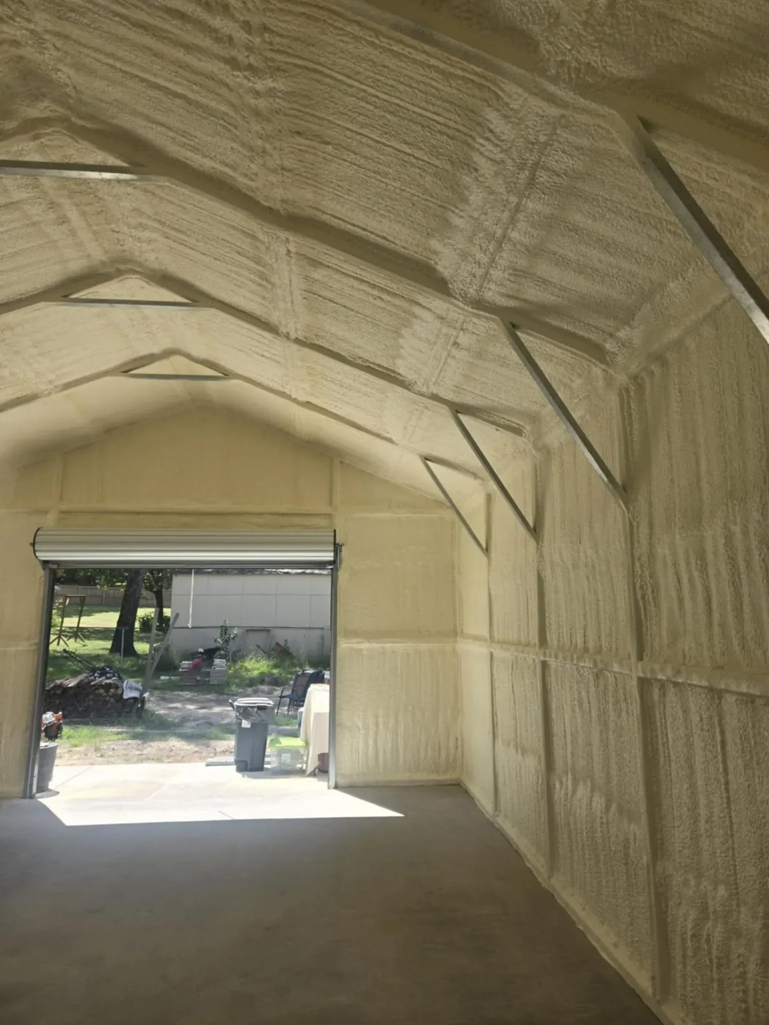 Interior of a building with spray foam insulation, open garage door with outdoor view. Beige color.