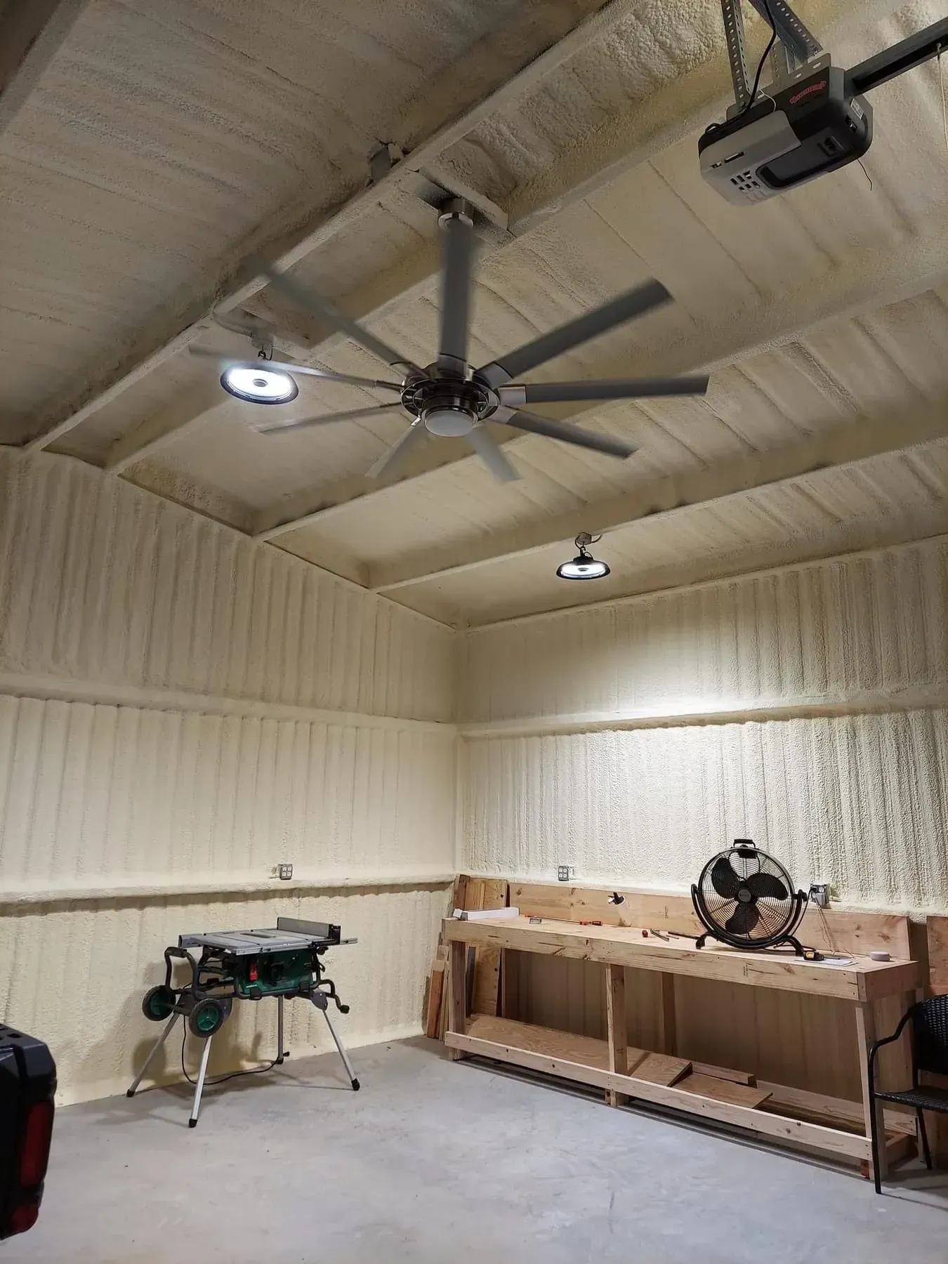 Garage interior with spray foam insulation, ceiling fan, work bench, and table saw.
