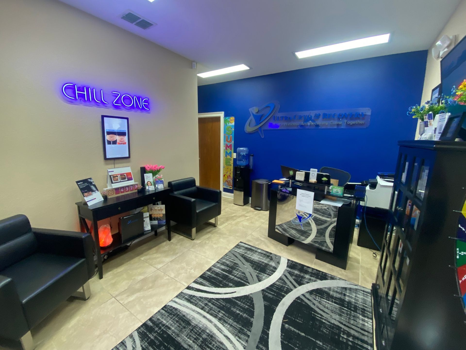 Waiting area of a business with black chairs, rug, and blue accent wall. Neon sign and water cooler visible.