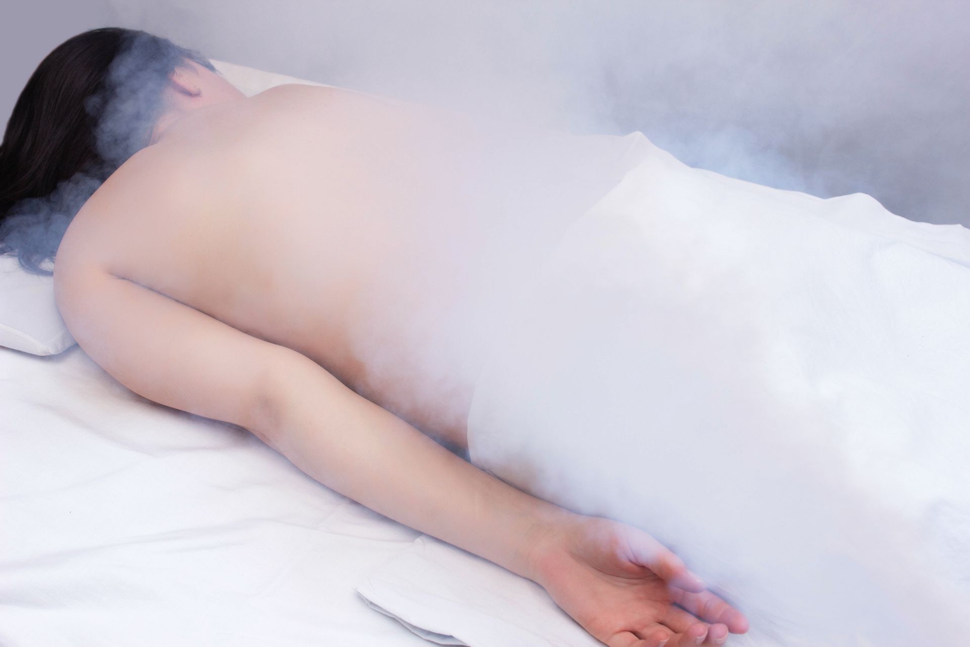 A person lies on a bed, partially obscured by vapor.