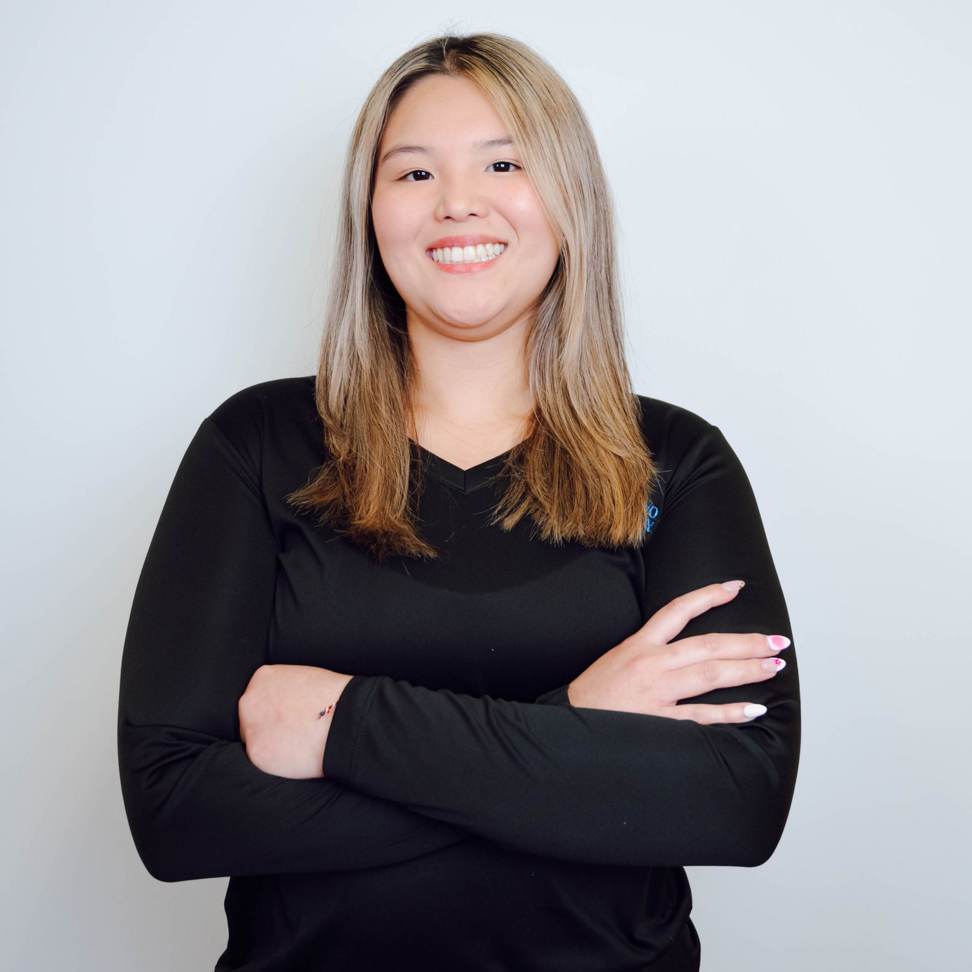 Woman in black long-sleeve shirt smiles, arms crossed. Against a white background.