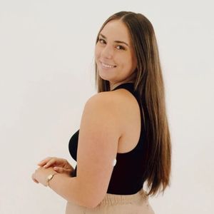 Woman with long brown hair in a black tank top and tan pants, smiling at the camera.
