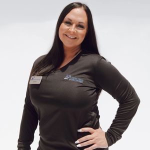 Woman in black long-sleeve shirt smiles, hand on hip, wearing a name tag. Against a white background.