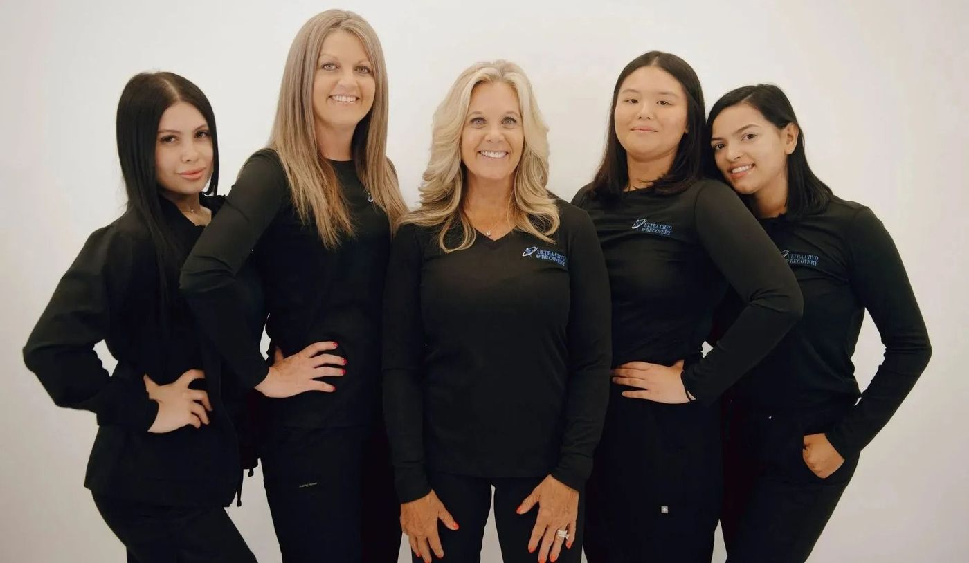 Five women in matching black shirts pose against a white backdrop, arms akimbo.